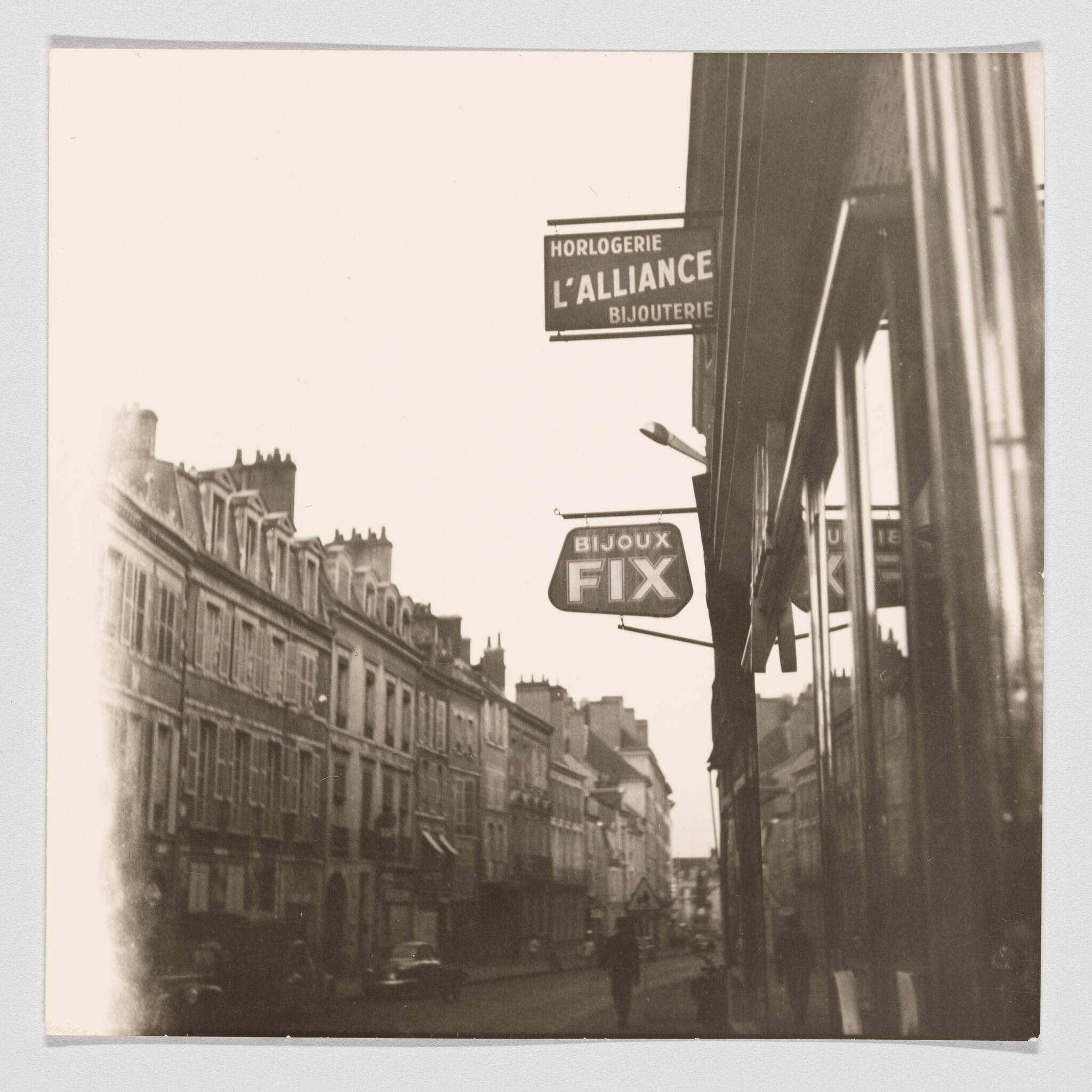 A narrow European street lined with buildings and jewelry shop signs reading L'Alliance and FIX.