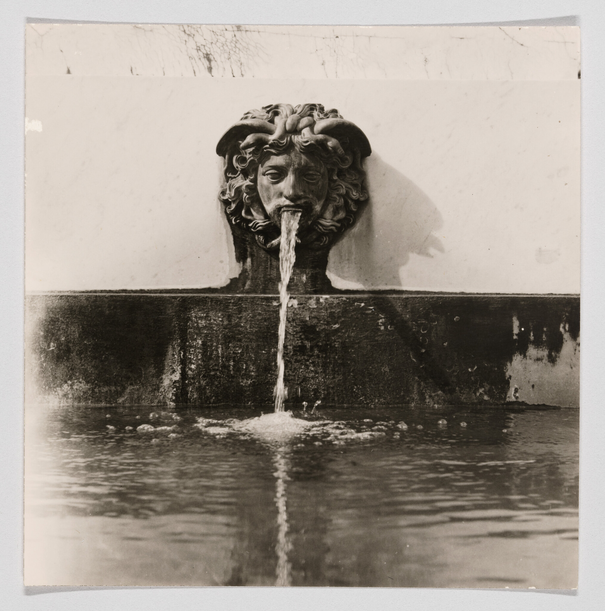 A carved stone face fountain spouts water into a pool below.