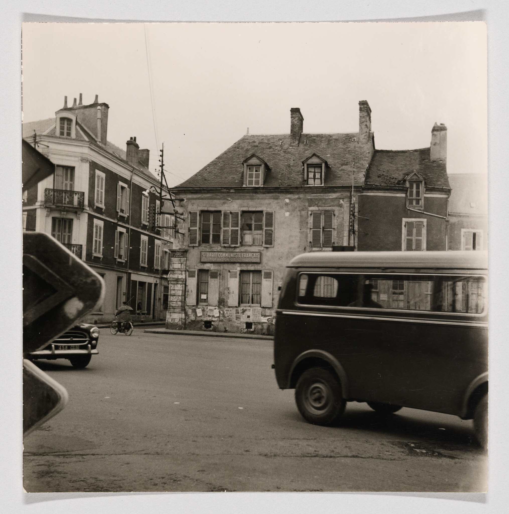 A worn building with a "Parti Communiste Français" sign as a van passes in the street.