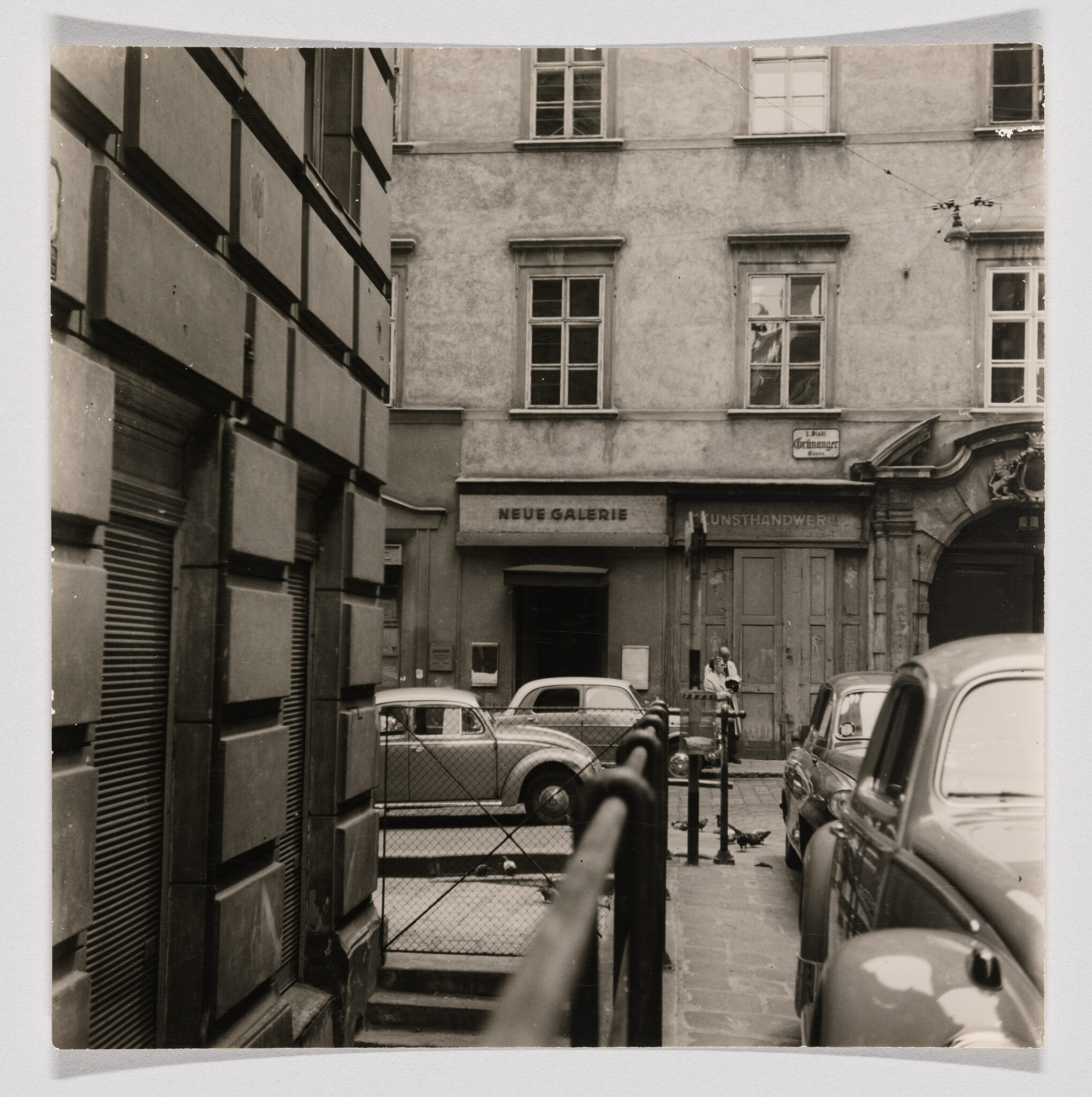 Narrow cobbled alley with parked vintage cars and the Neue Galerie entrance in the background.