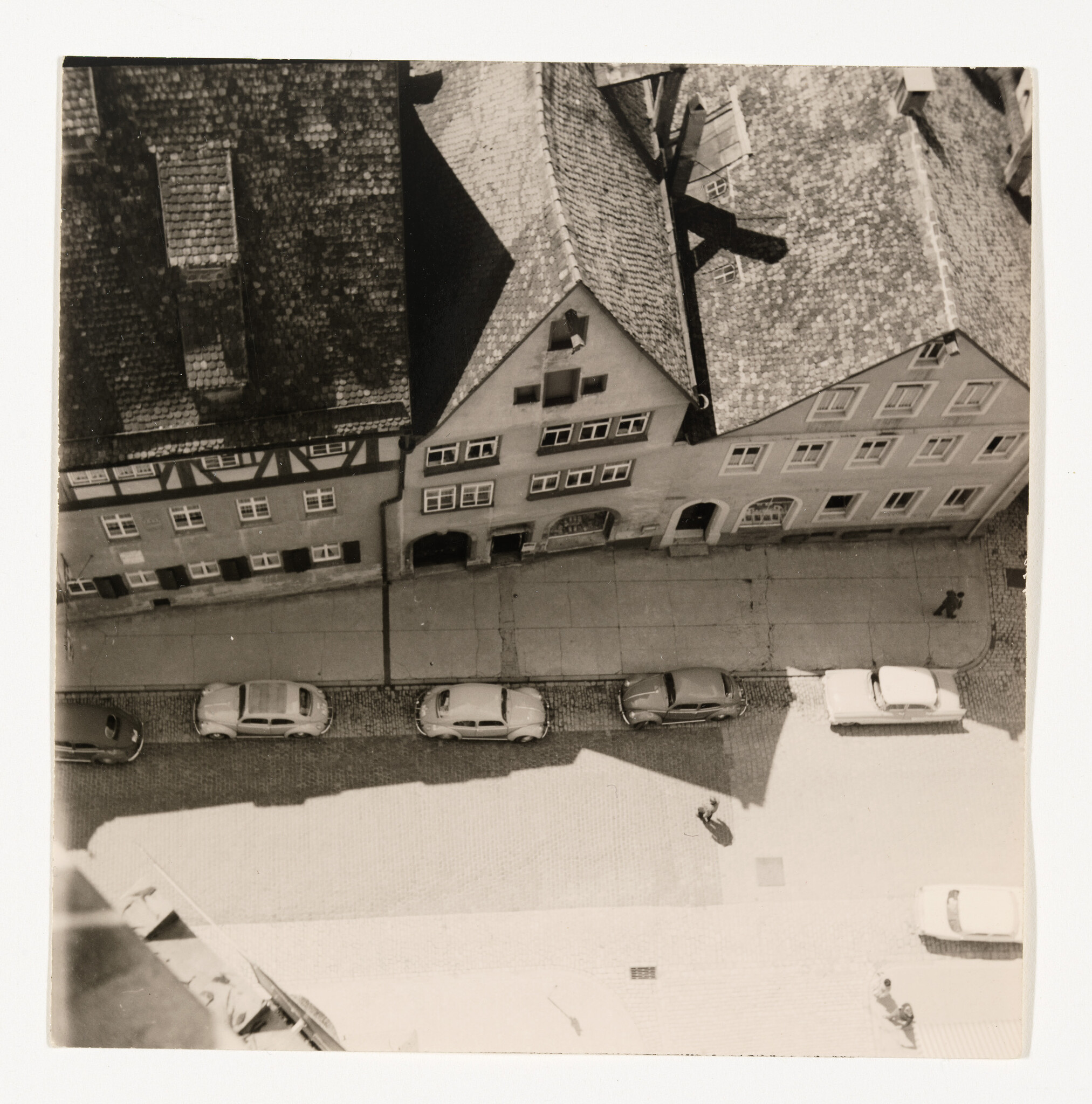 Aerial view of a narrow street with parked cars and two pedestrians walking.