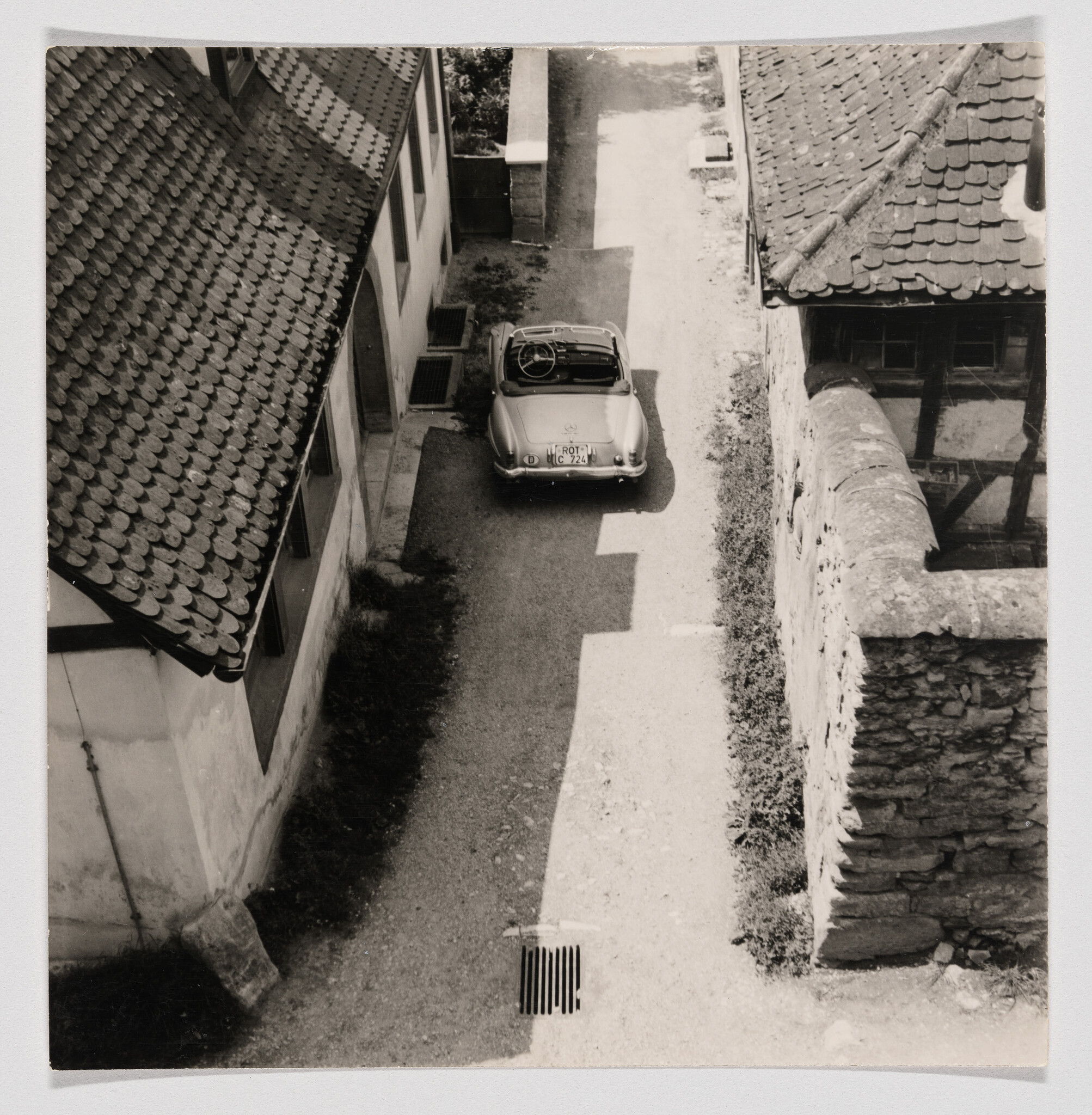 A vintage convertible car is parked in a narrow alley between old buildings.