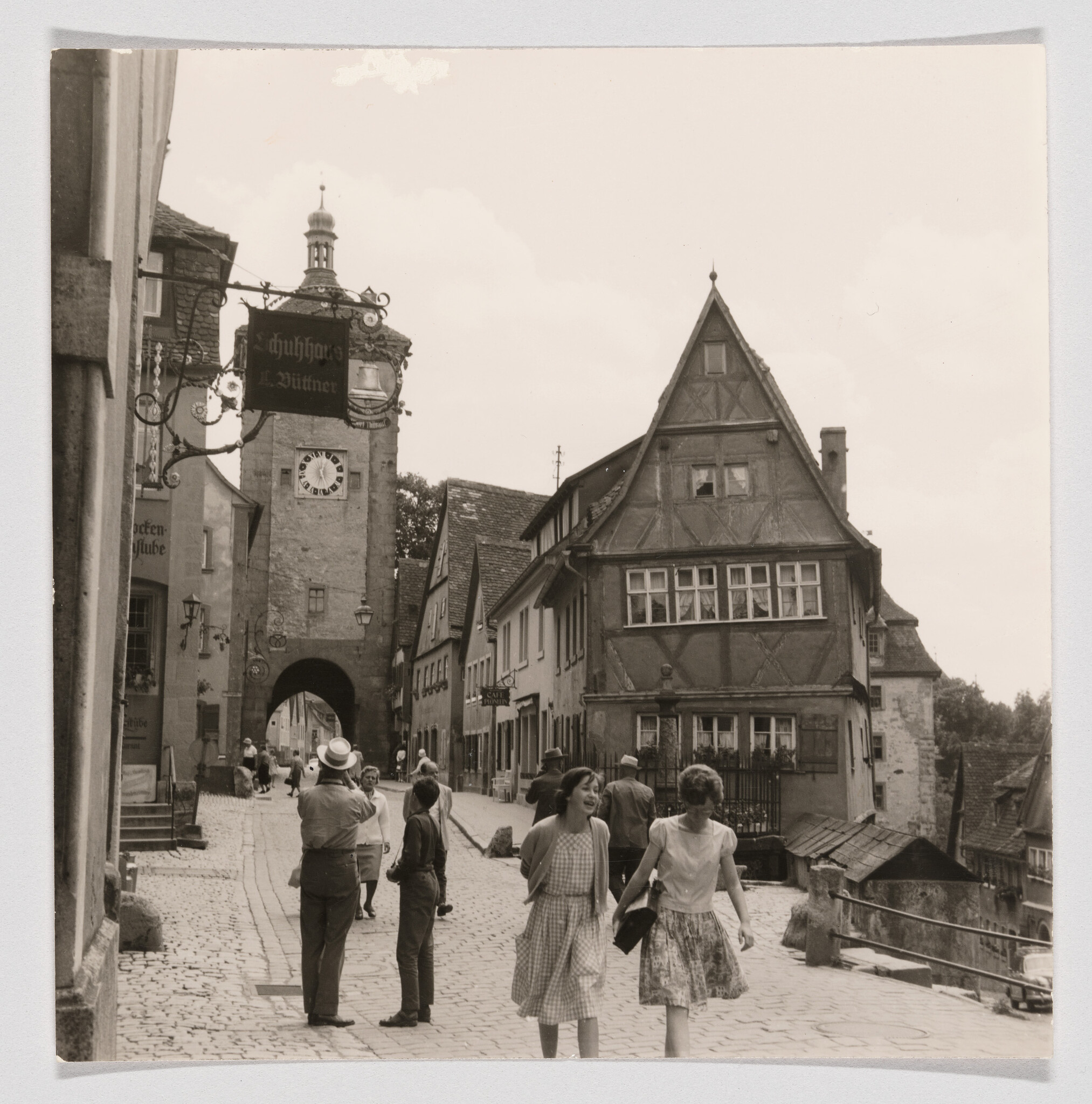 Two young women walk and laugh along a cobblestone street past a clock tower arch.