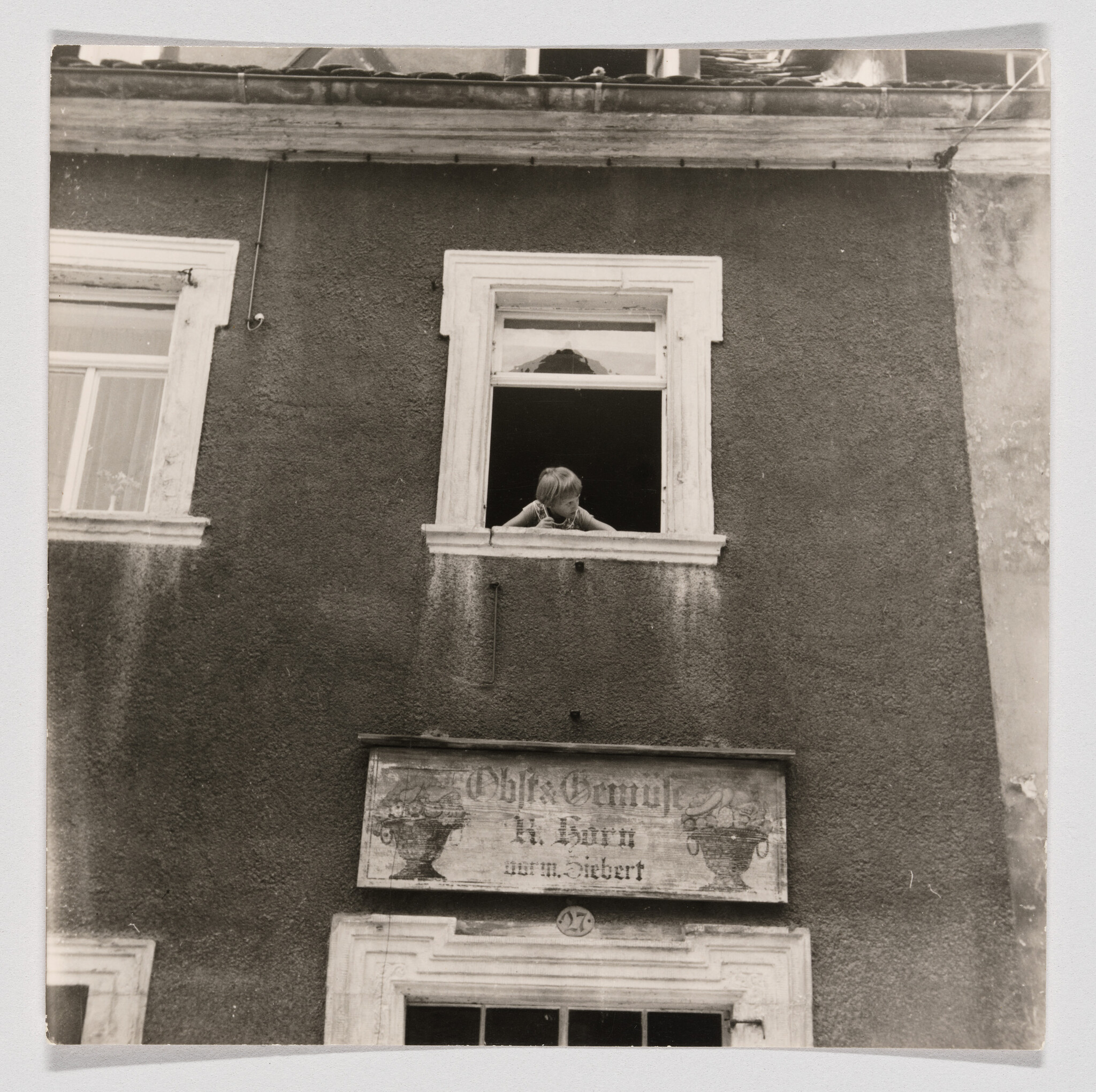 A child leans out of a second-floor window looking down the street.