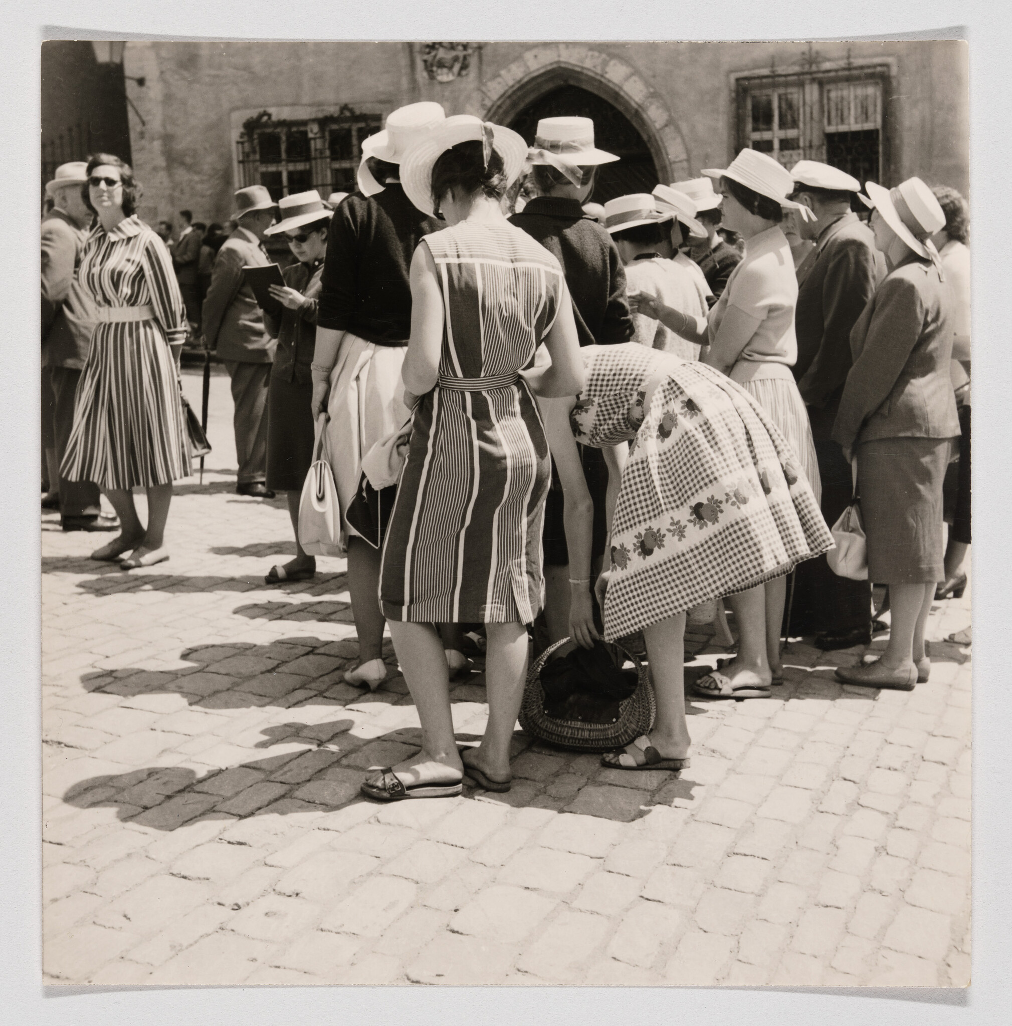 A group of women in sun hats stand together while one bends to reach into a basket.
