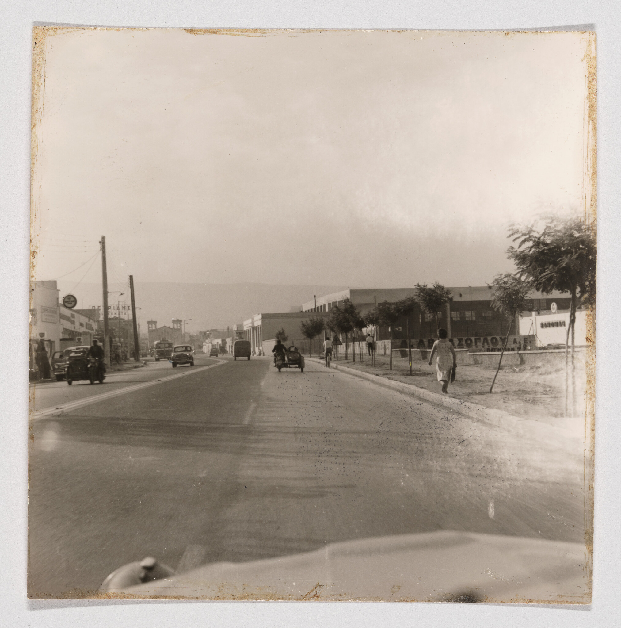 A wide street with vintage cars, a motorcycle sidecar, and pedestrians on the sidewalk.