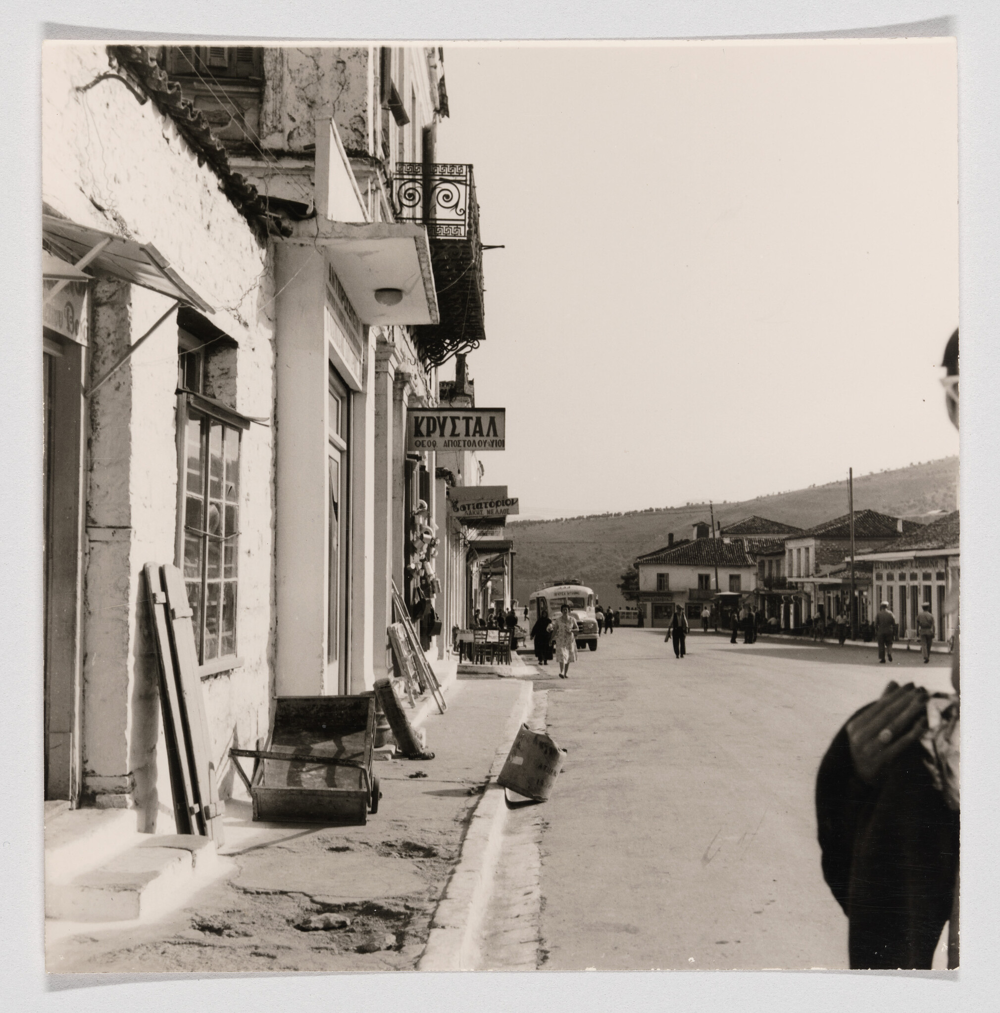 A quiet main street with shops, pedestrians walking along the sidewalk, and a bus approaching in the distance.