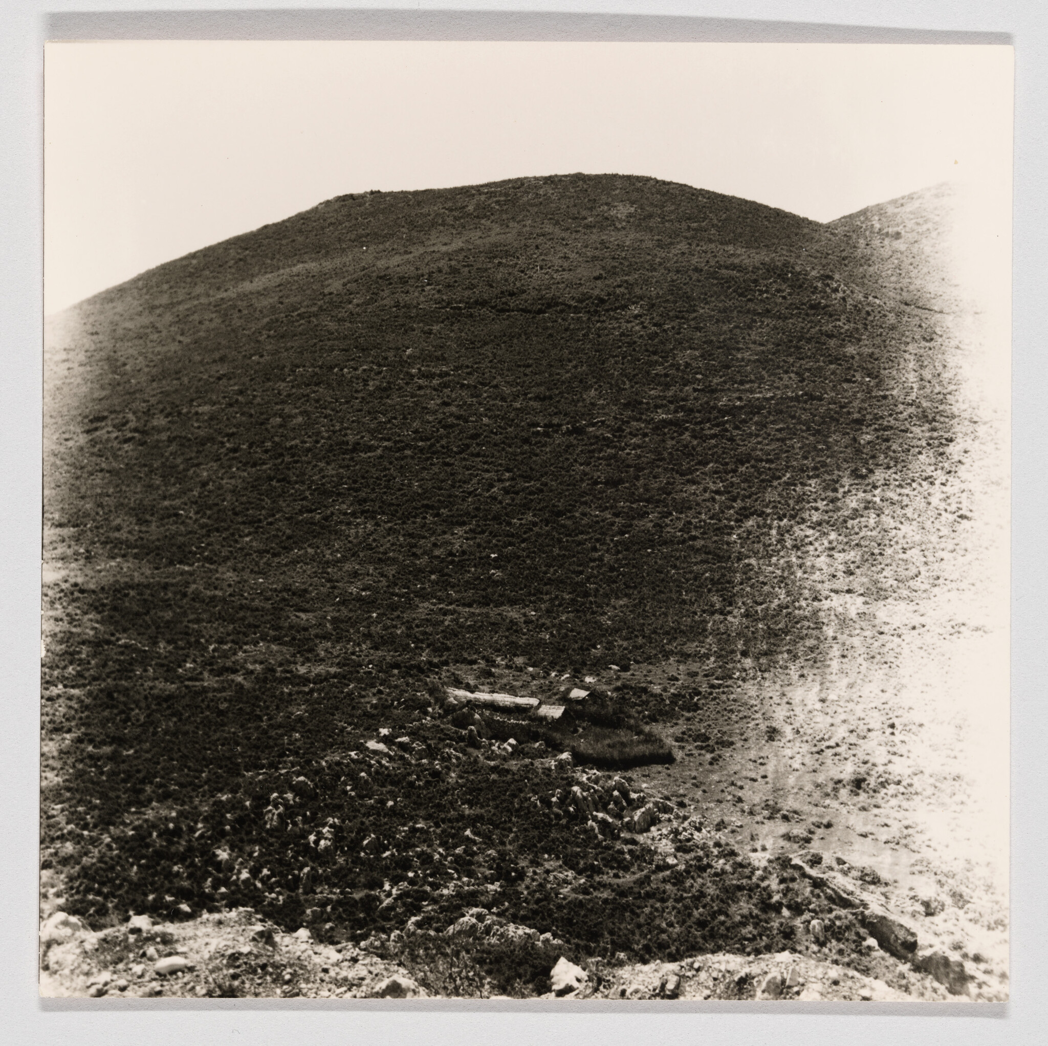 Small stone ruins lie at the base of a large, sparsely vegetated hillside.