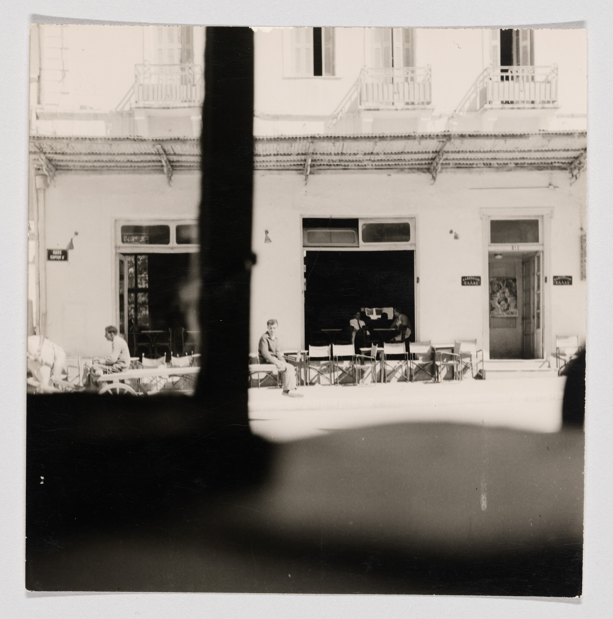 Man sitting on a row of sidewalk café chairs in front of a building.