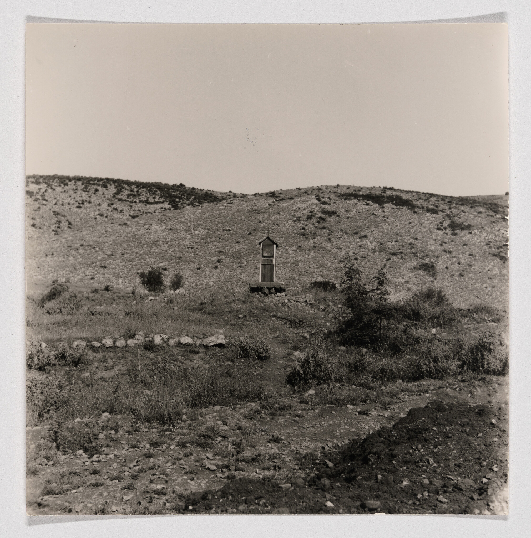 Small wooden shrine stands alone on a rocky plain with low hills behind.