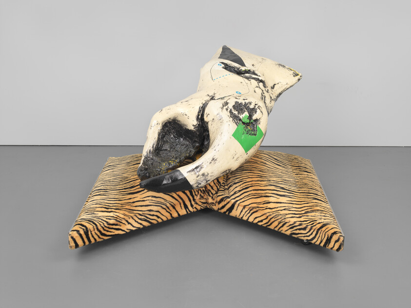A worn white and black abstract torso sculpture with a green patch resting on tiger-striped cushions.