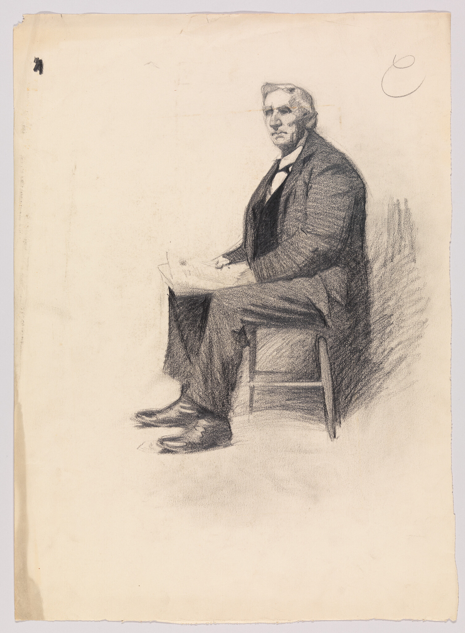 An older man in a suit sits on a stool holding papers and looking forward.