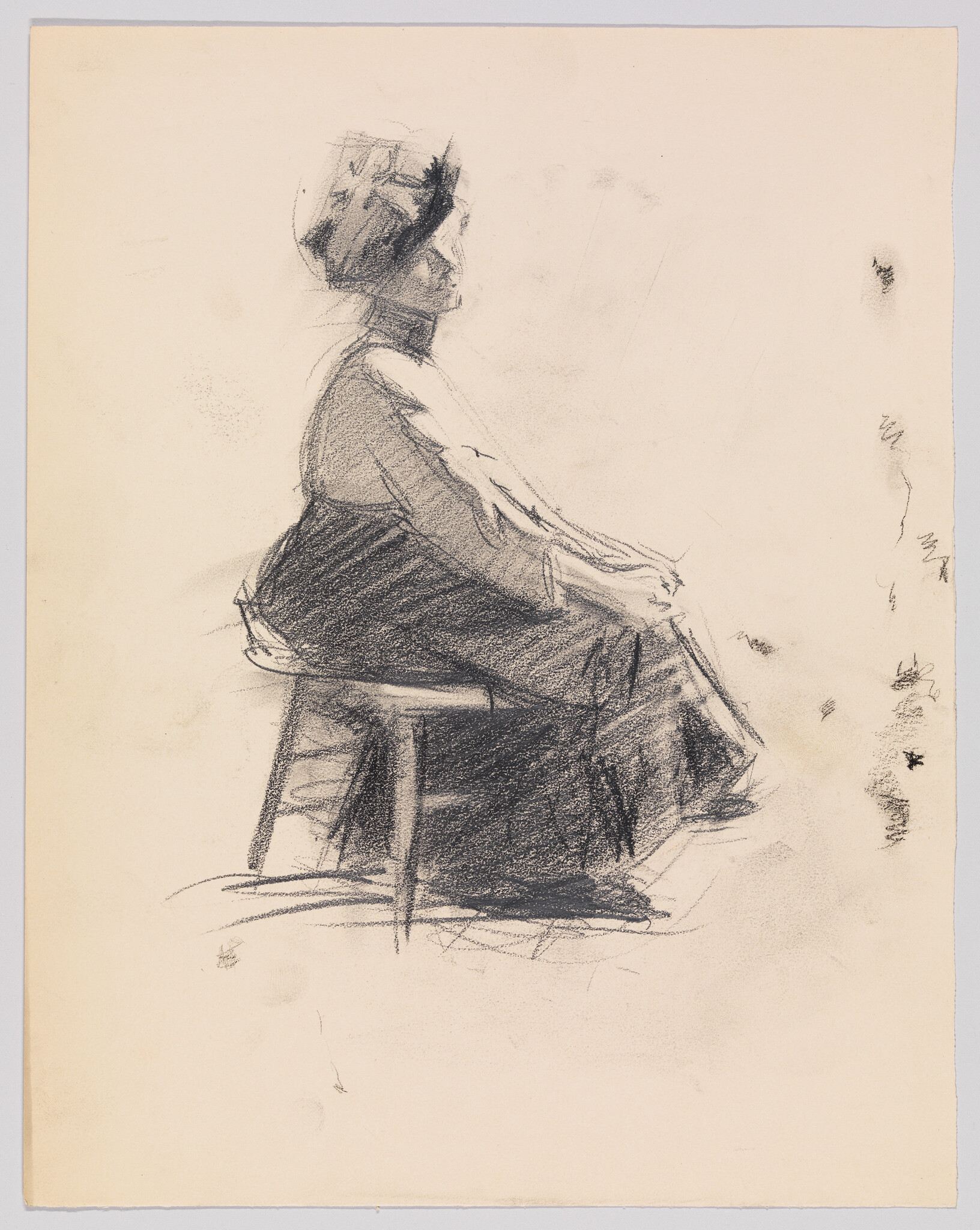 A woman in profile wearing a hat sits on a stool with hands clasped.