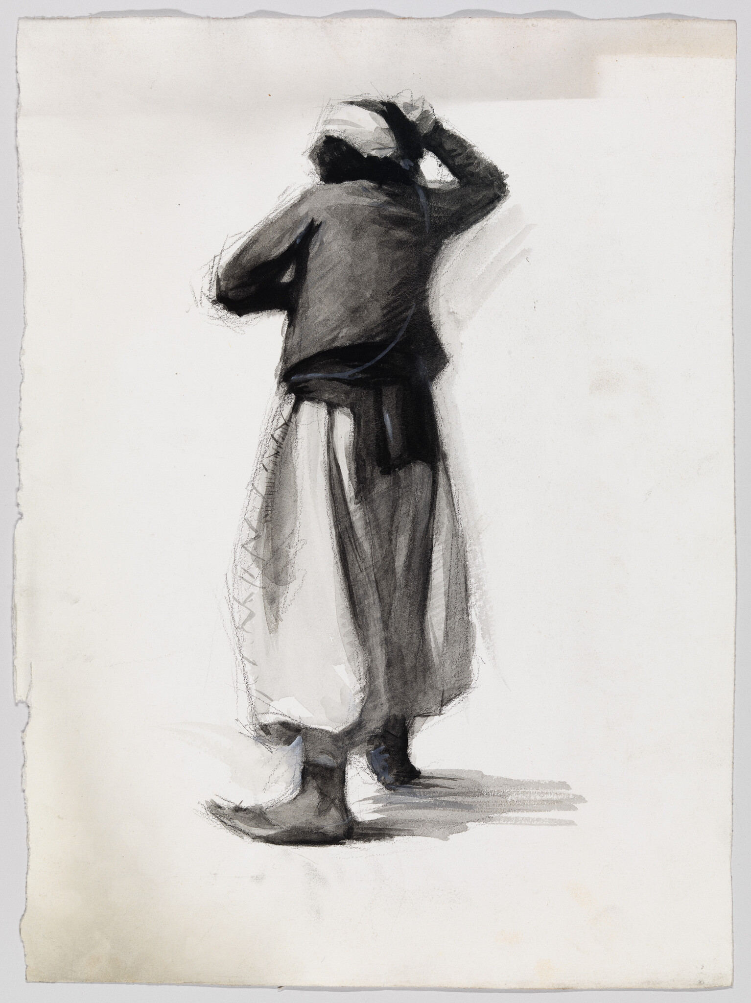A person seen from behind adjusts a headscarf while wearing a long skirt and boots.