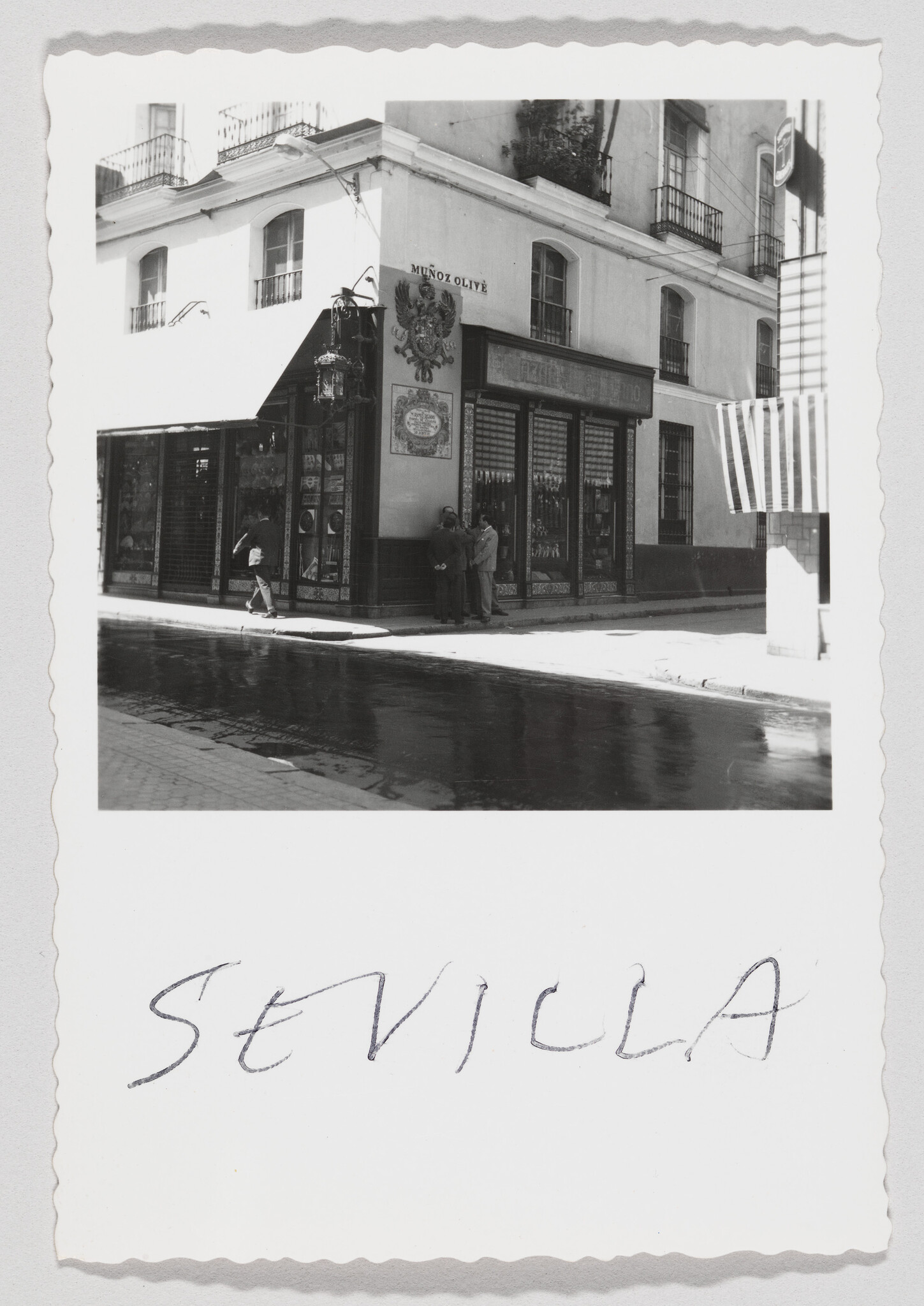 Corner shop in Seville with three men talking by the window and a passerby walking.