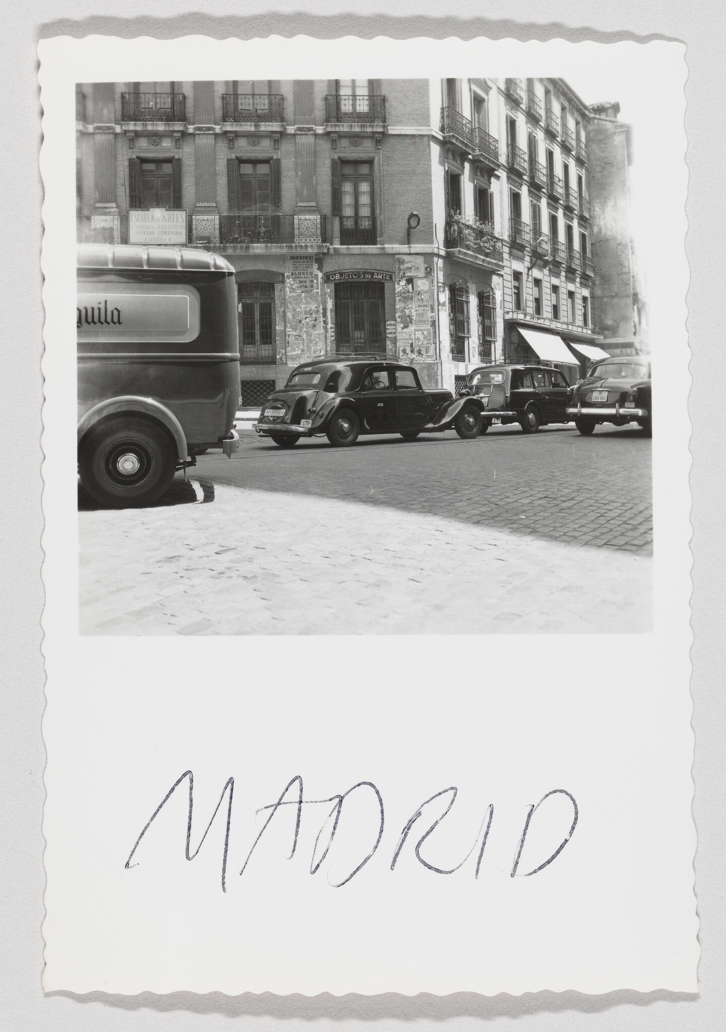 Several vintage cars parked along a cobblestone Madrid street beneath old apartment buildings.