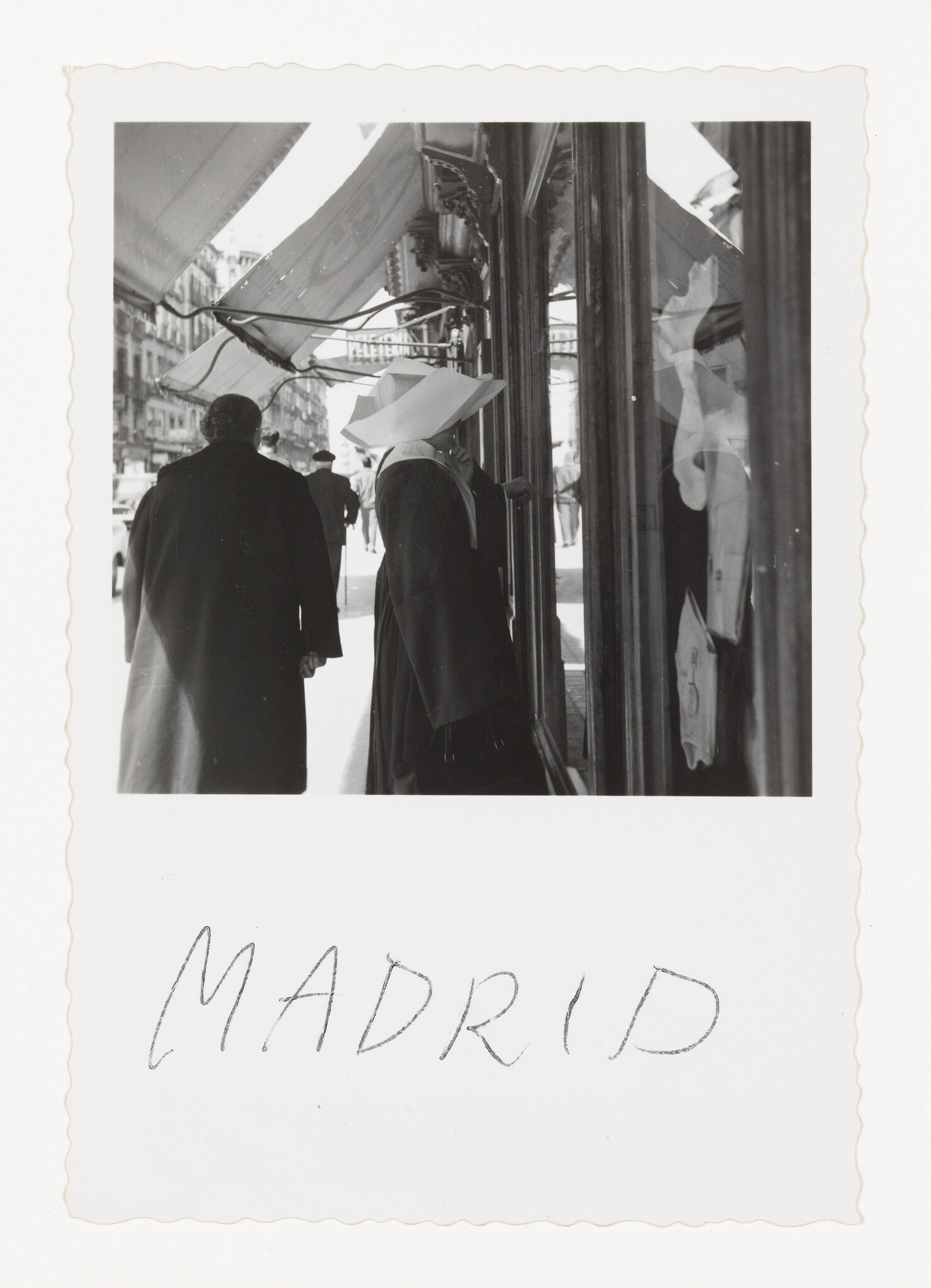 A nun in a white cornette looks into a shop window on a busy Madrid street.