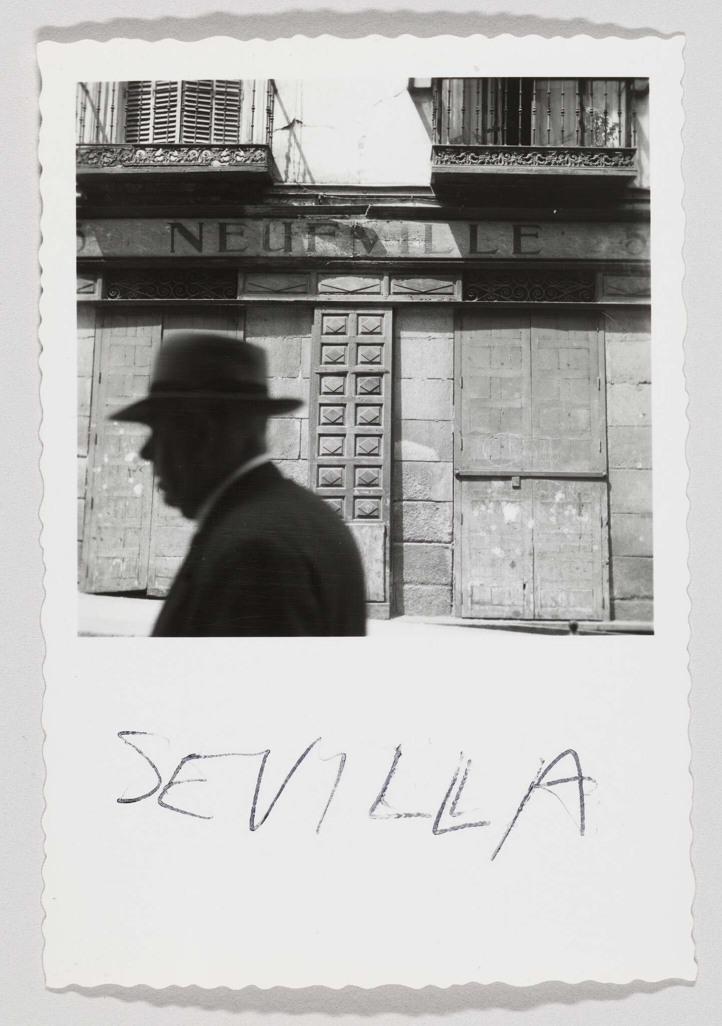 Silhouetted man in a hat walking past a closed storefront with "Sevilla" written below.