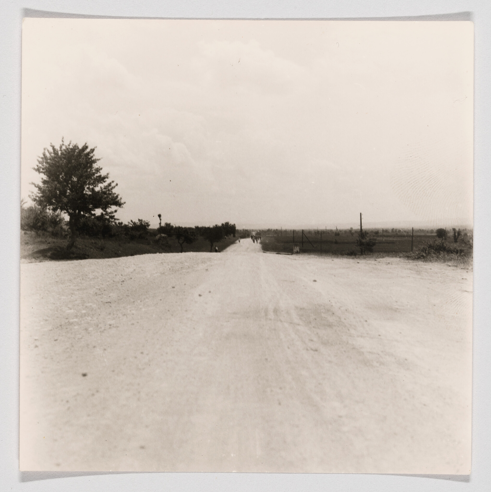 A wide dusty country road stretches toward the horizon with a few distant walkers.