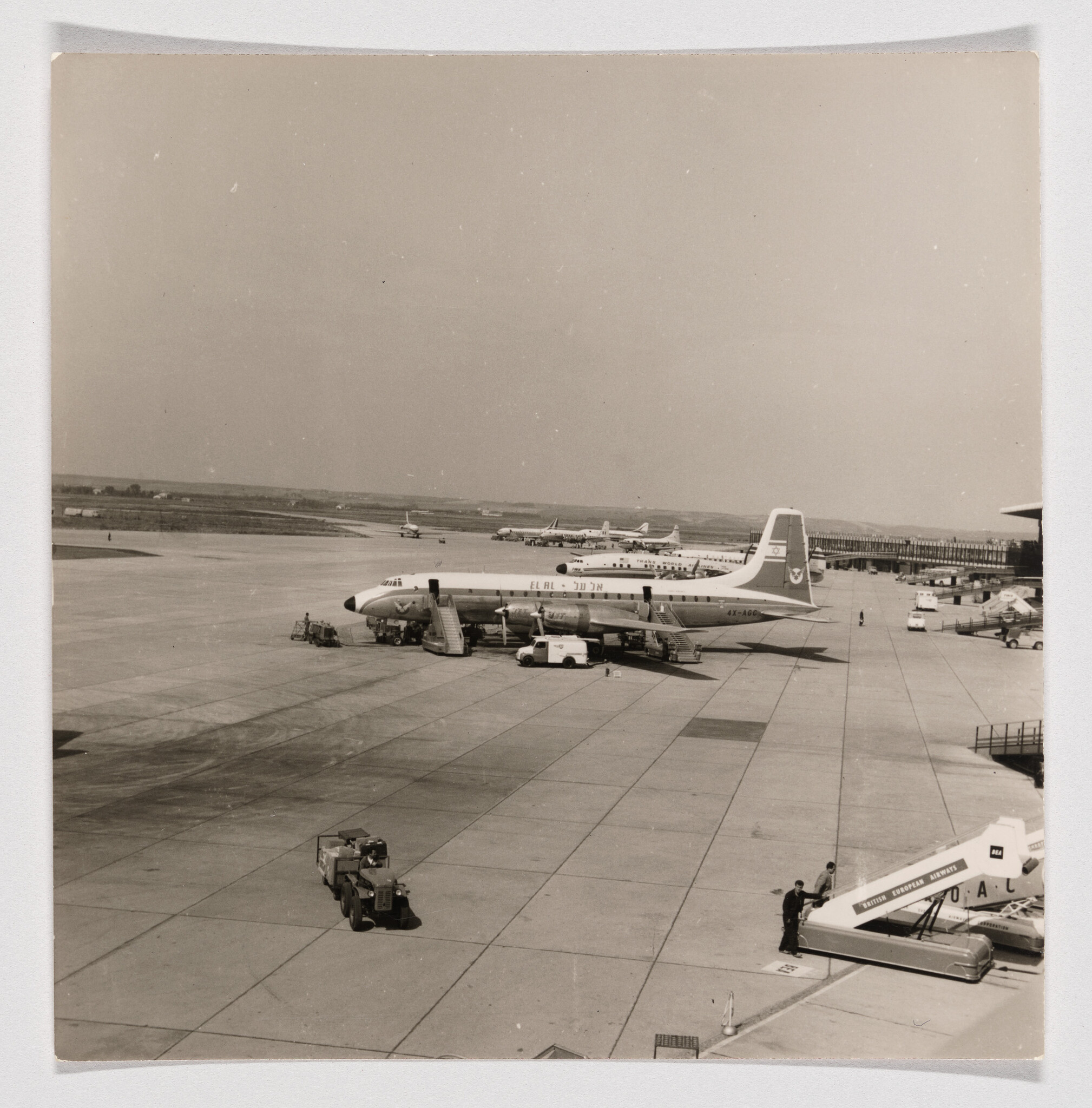 A passenger plane parked at the airport with boarding stairs and ground vehicles nearby.
