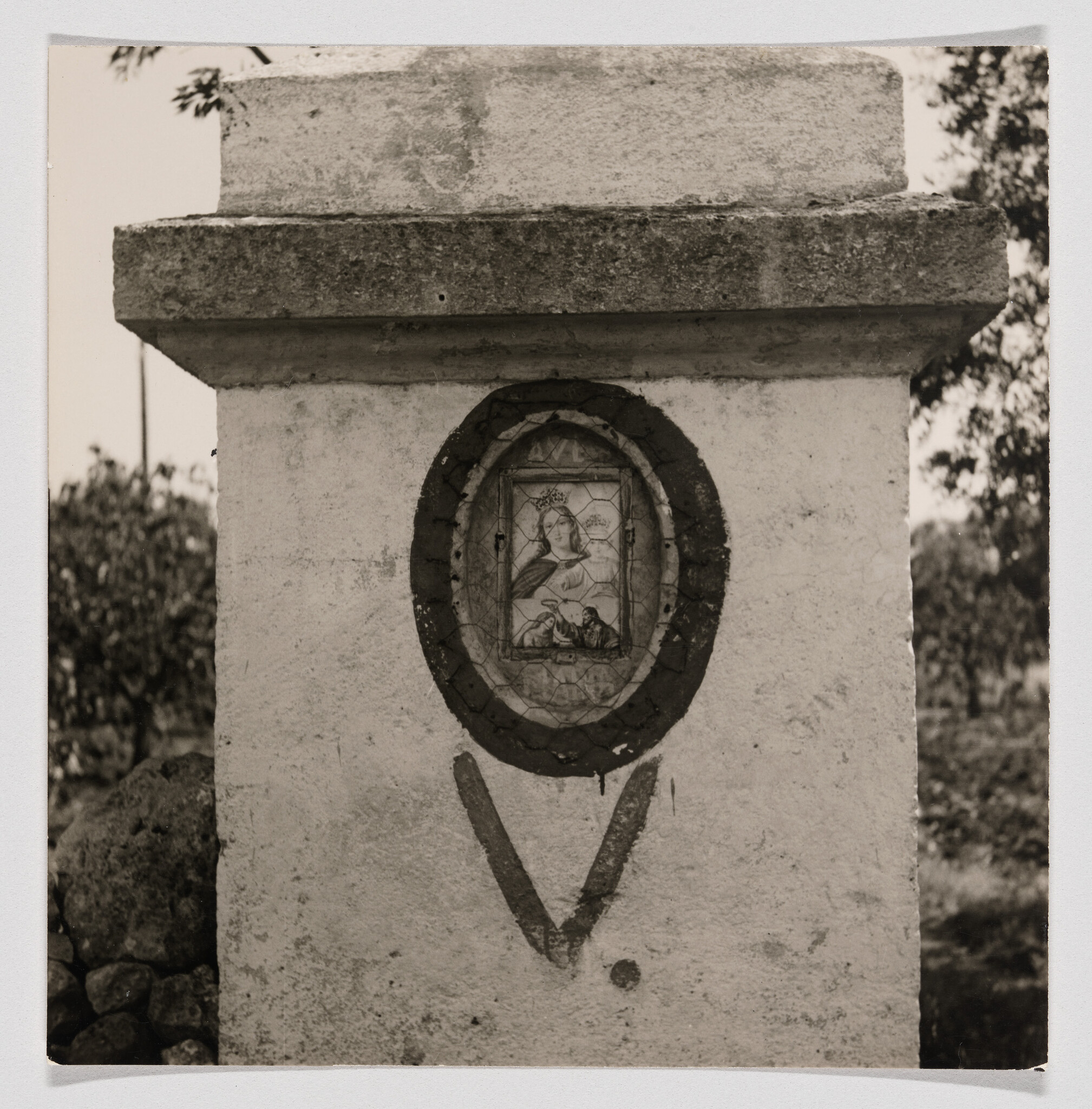 A small framed religious image of the Virgin is set into a weathered roadside stone pillar.
