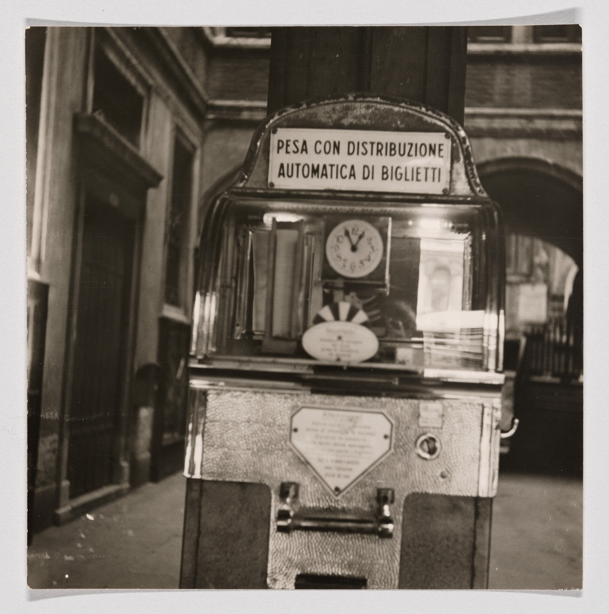Old coin-operated weighing machine with automatic ticket dispenser standing in a narrow corridor.
