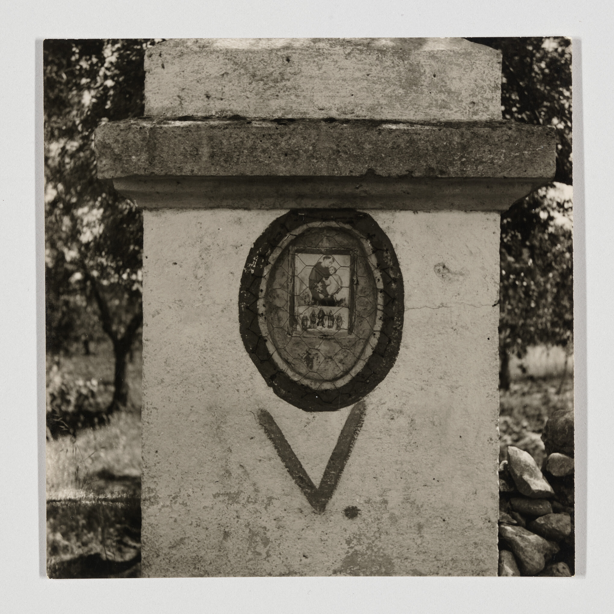 A small white roadside shrine with an oval framed religious picture and a painted V.