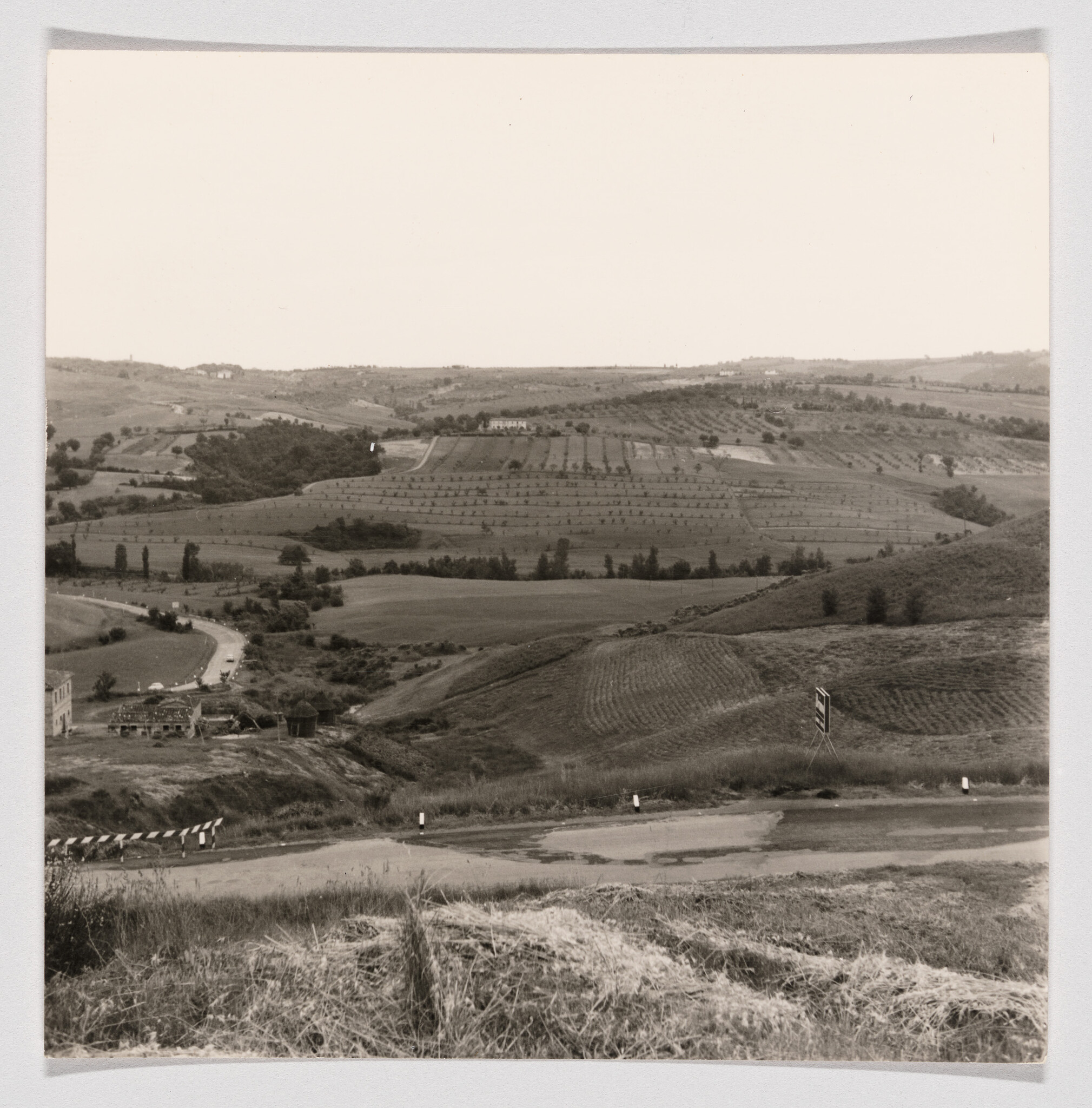 Rolling farmland and orchards spread across hills with a winding road and roadside barriers.