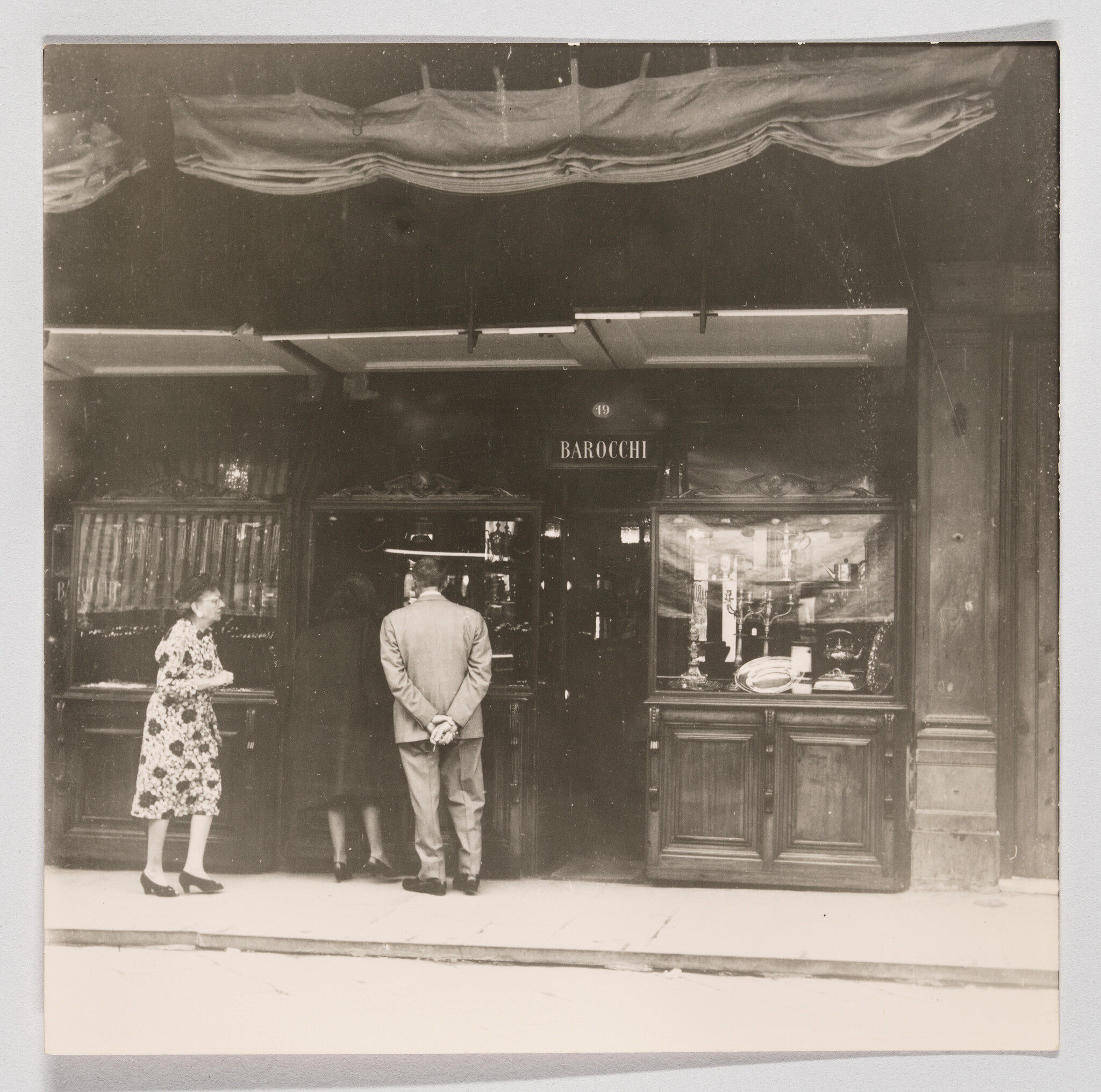 Three people stand at the entrance of Barocchi shop, two looking inside and one watching.