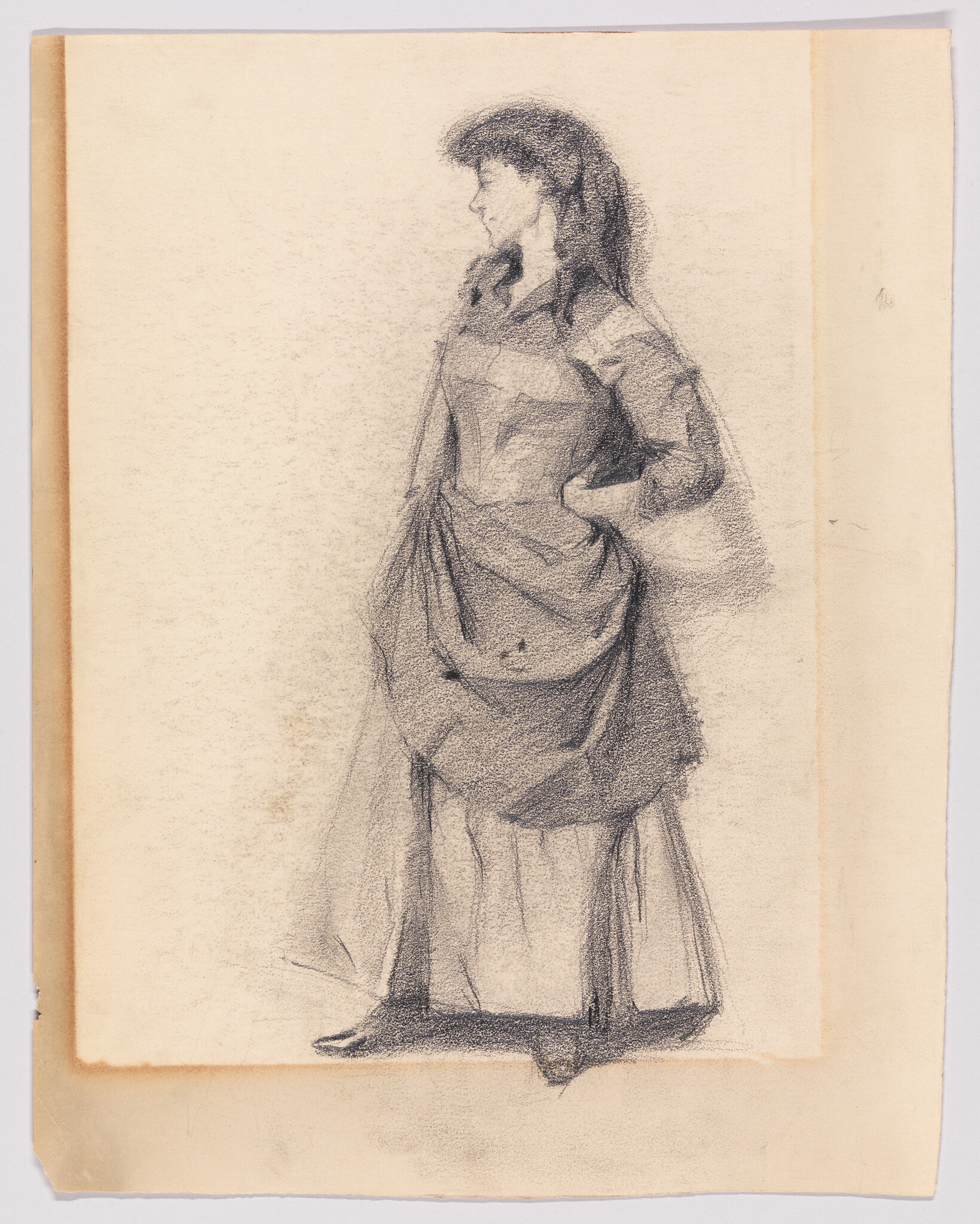 A standing woman in a long dress looks to the left with her hands on her hips.