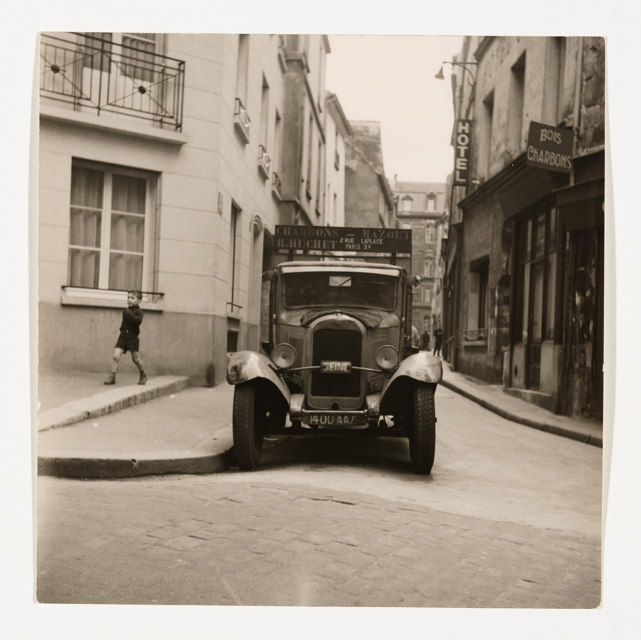 A vintage delivery truck parked on a narrow Paris street while a boy walks on the sidewalk.