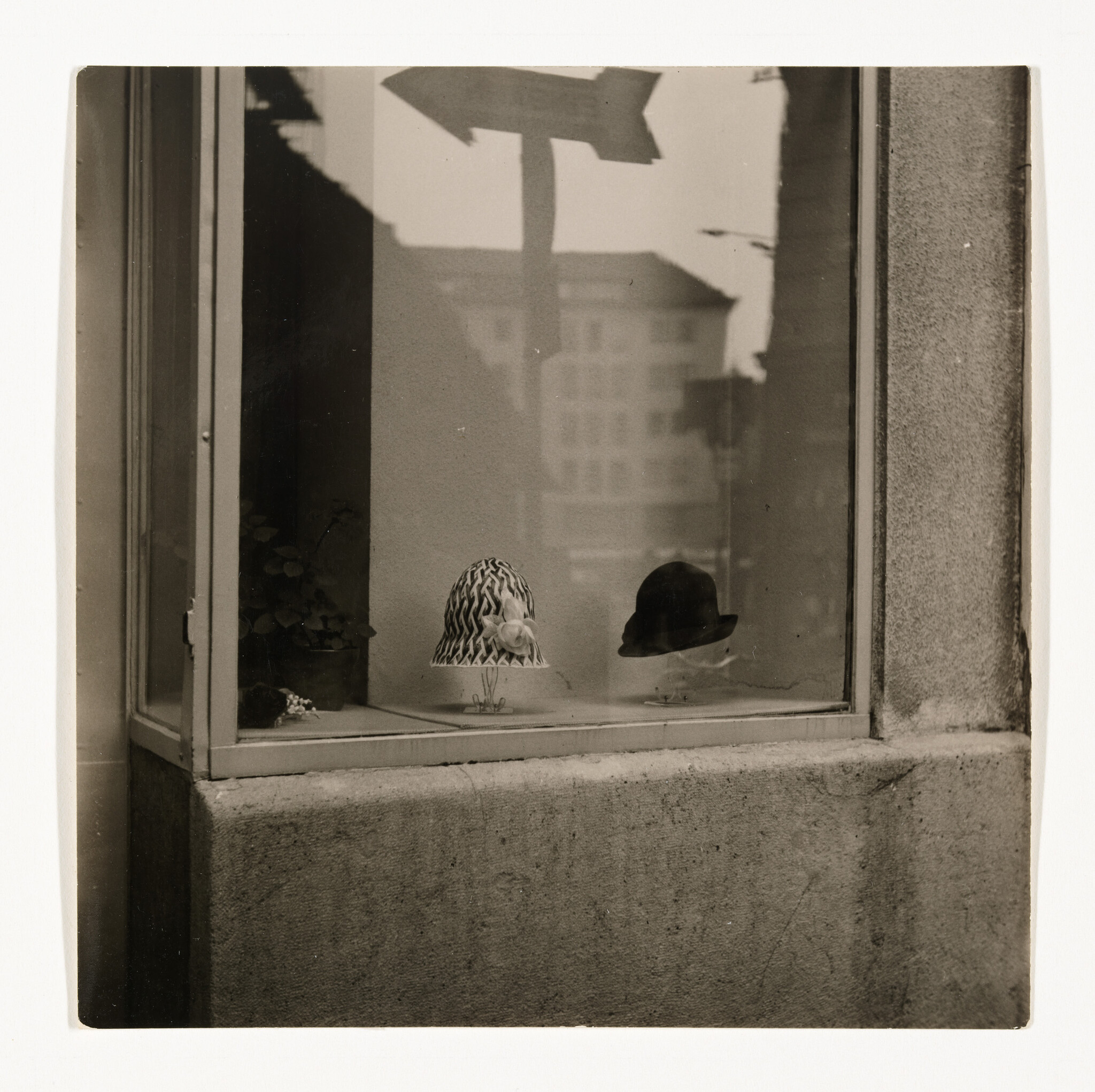 Two women's hats, a patterned cloche with flower and a dark bowler, sit in a shop window.
