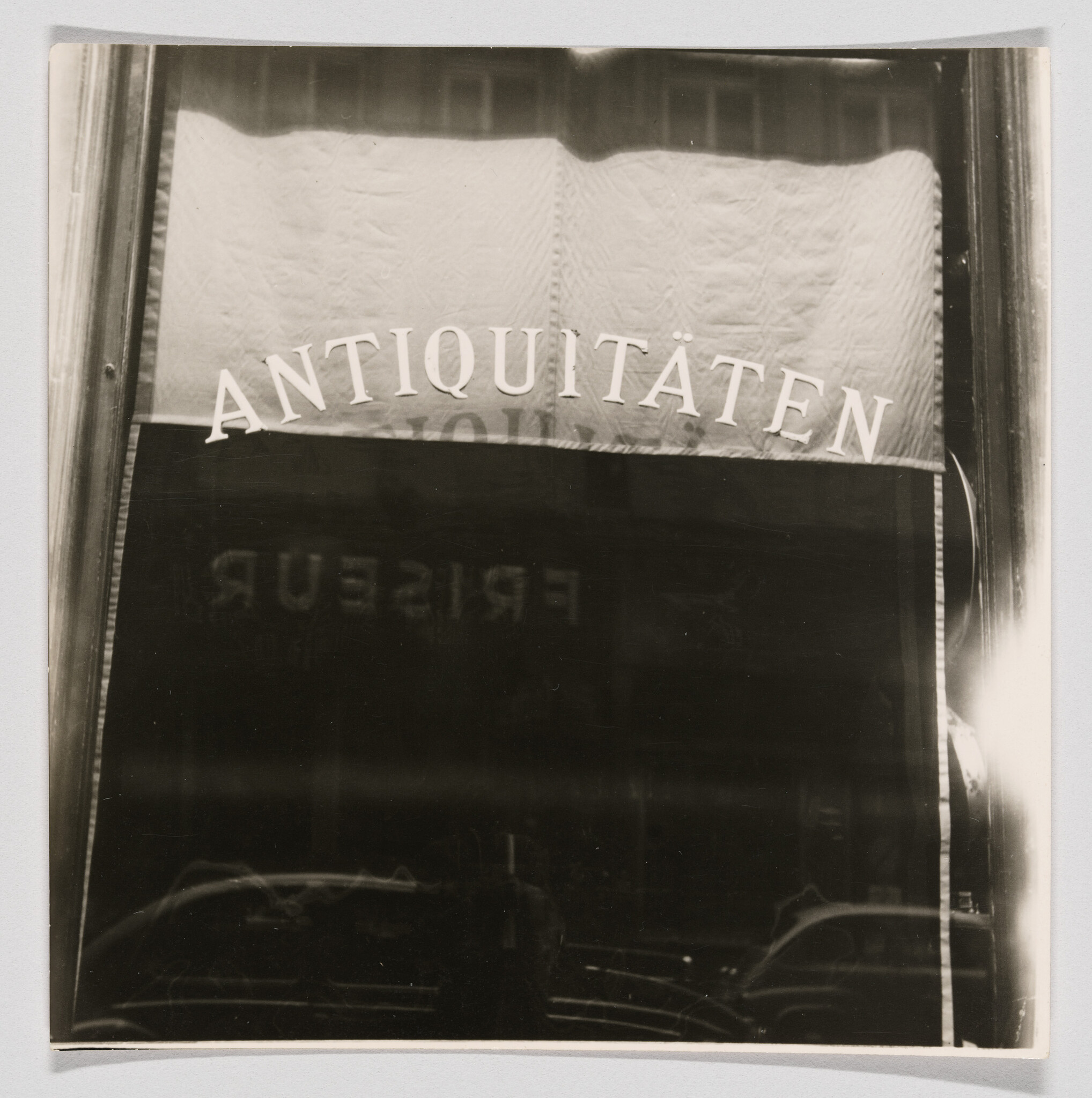 Shop window with the word Antiquitäten painted across the top and dark interior reflection.