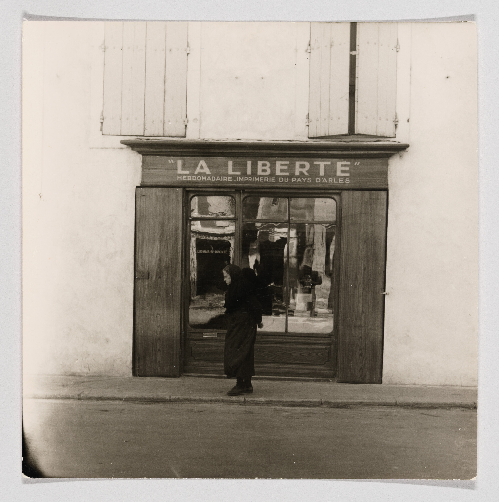An elderly woman walks past the shopfront marked "La Liberté" with reflective window panes.