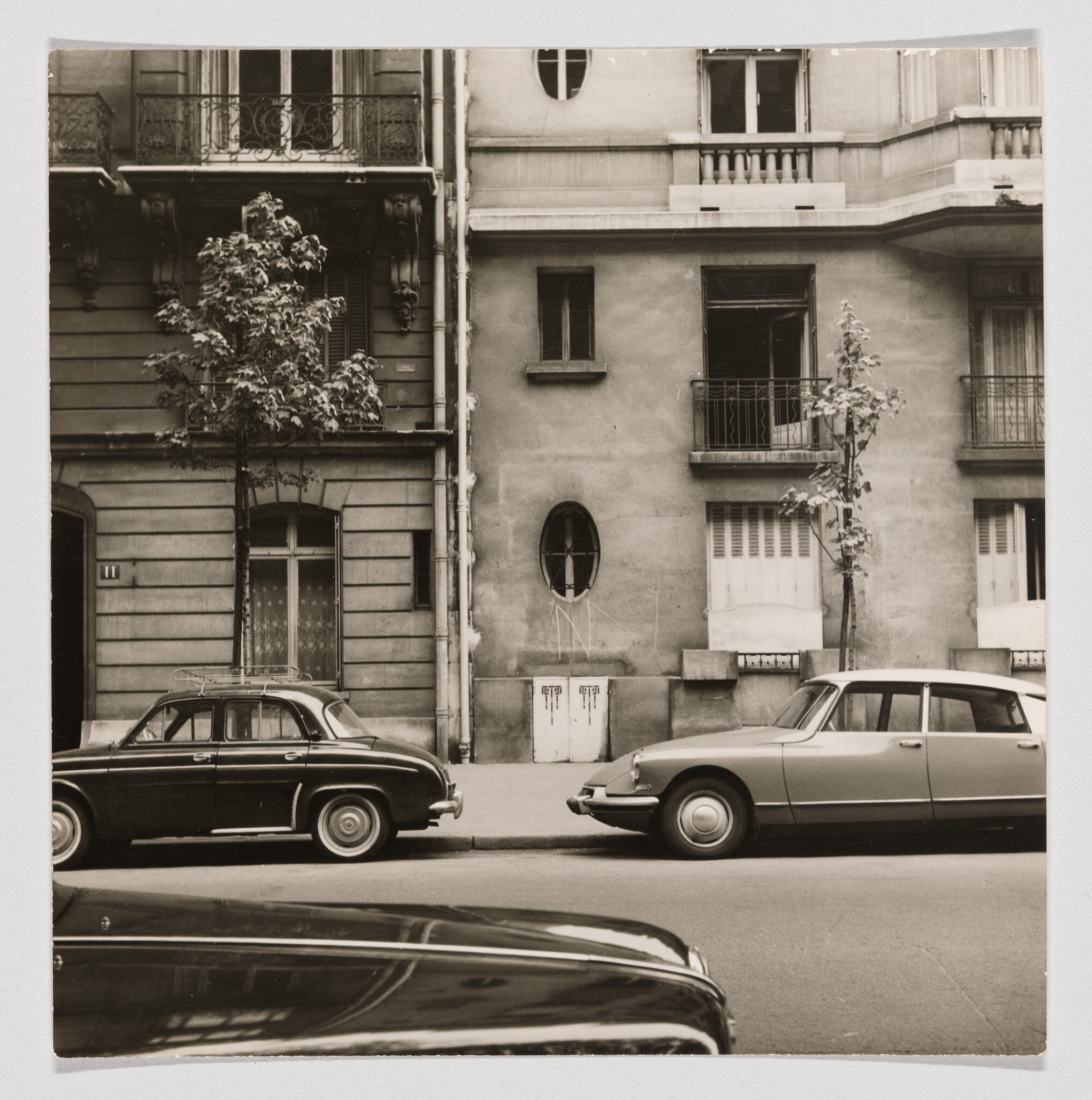 Two vintage cars parked along a quiet city street in front of an old apartment building.