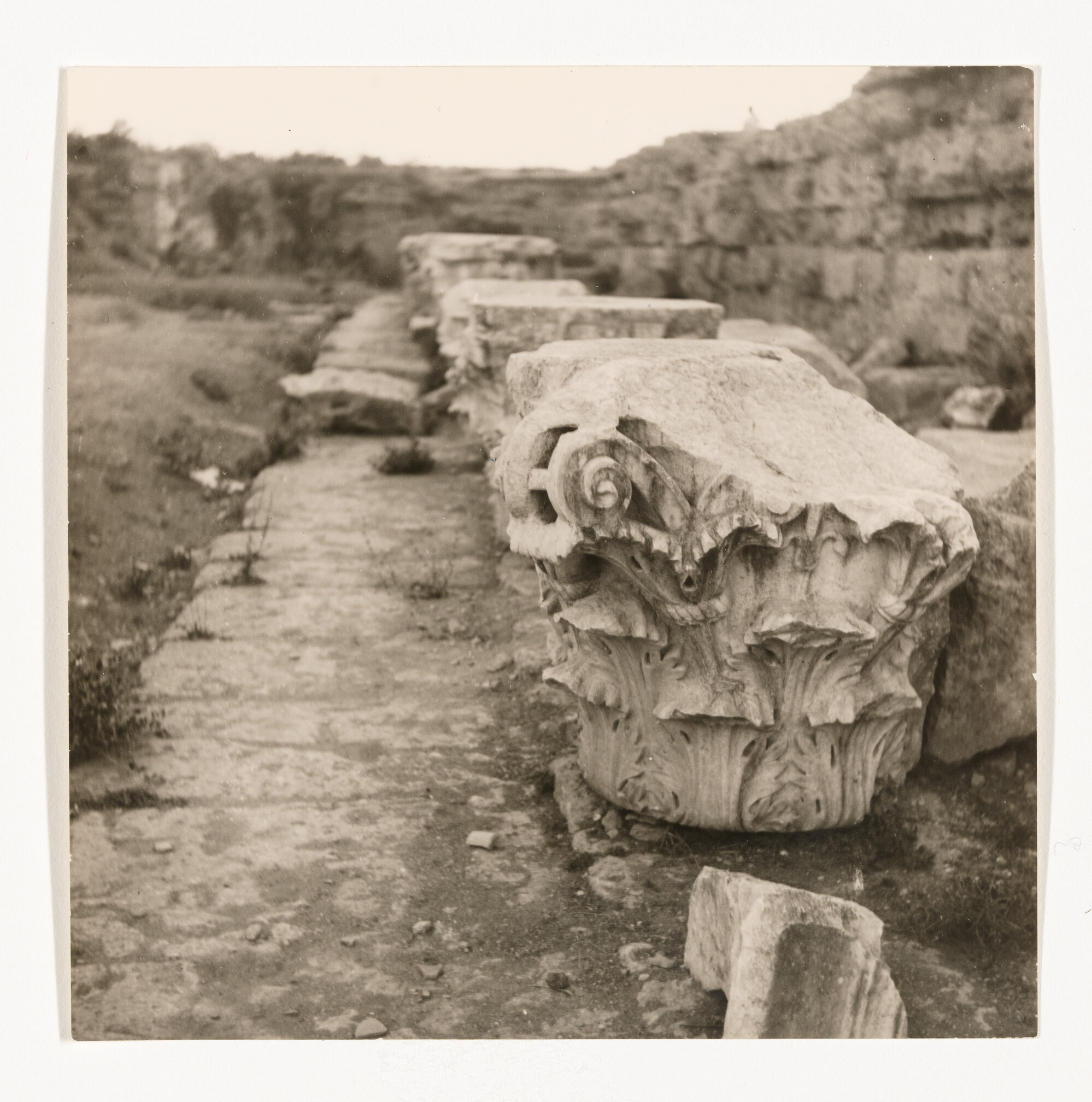 Carved stone column capitals lie in a row along an ancient ruined stone pathway.