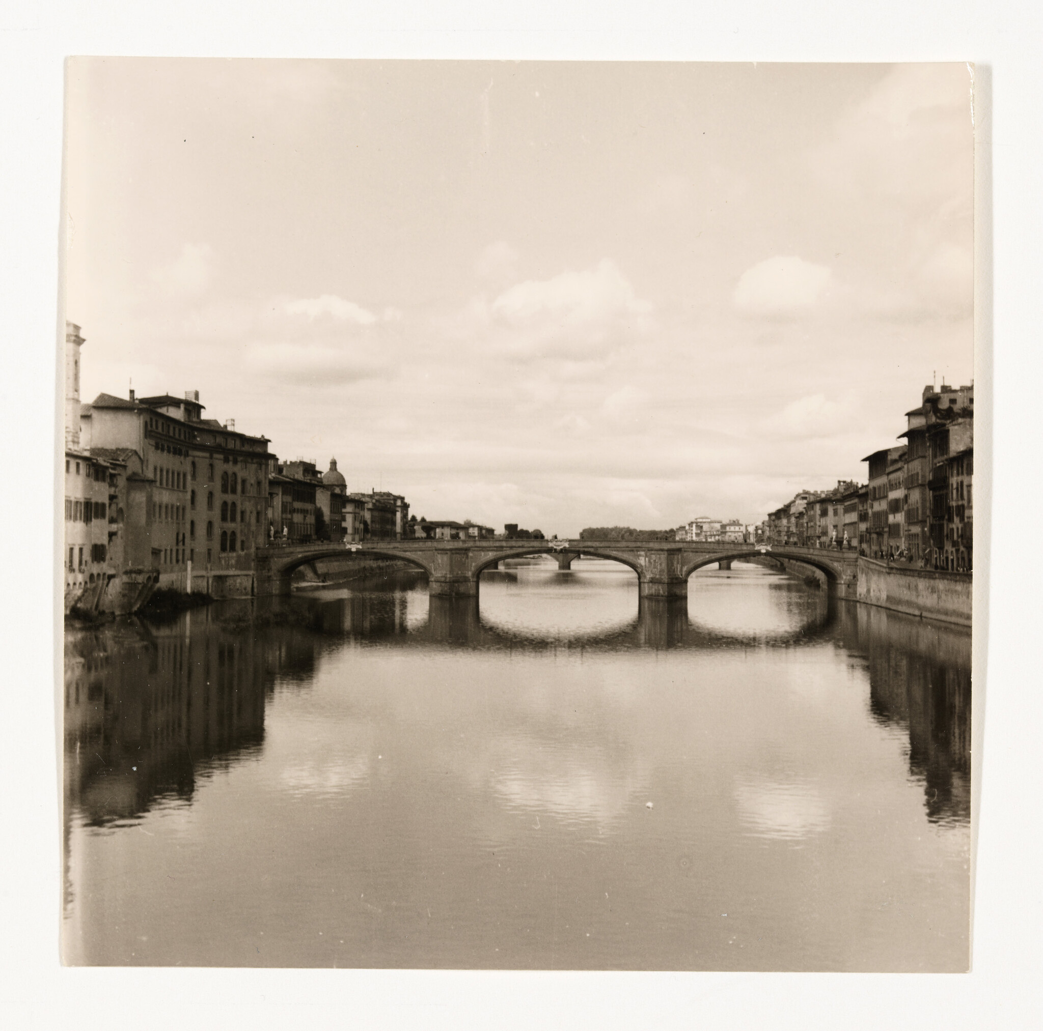 A stone arch bridge spans a calm river with old buildings and their reflections.
