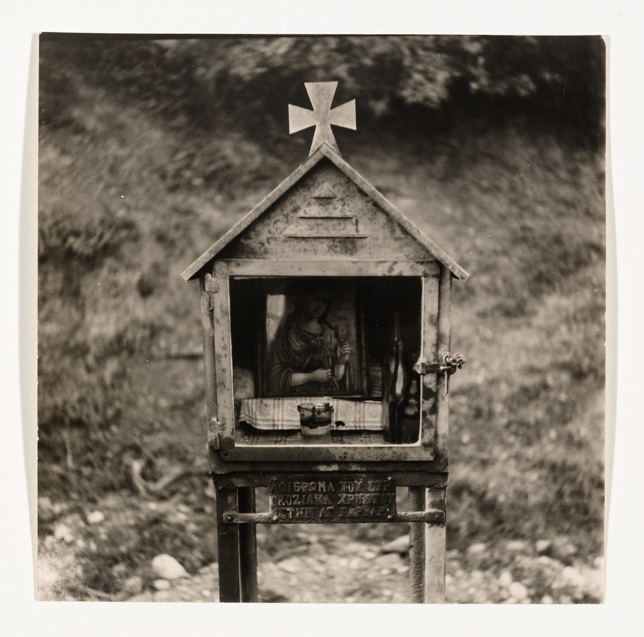 Small roadside shrine with a Christian icon, a cross on top, candles and a bottle inside.