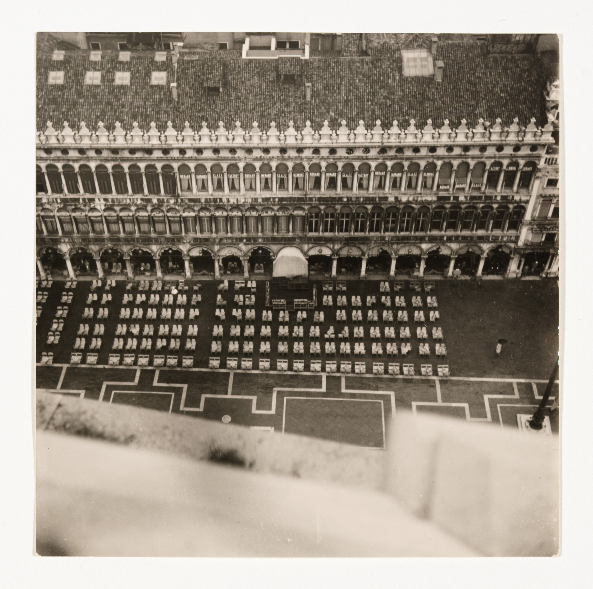Aerial view of a large plaza with rows of outdoor tables and chairs in front of an ornate building.