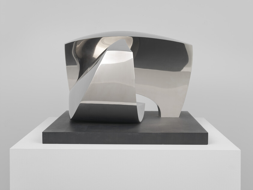 A polished stainless steel abstract sculpture with curved openings sits on a black base pedestal.