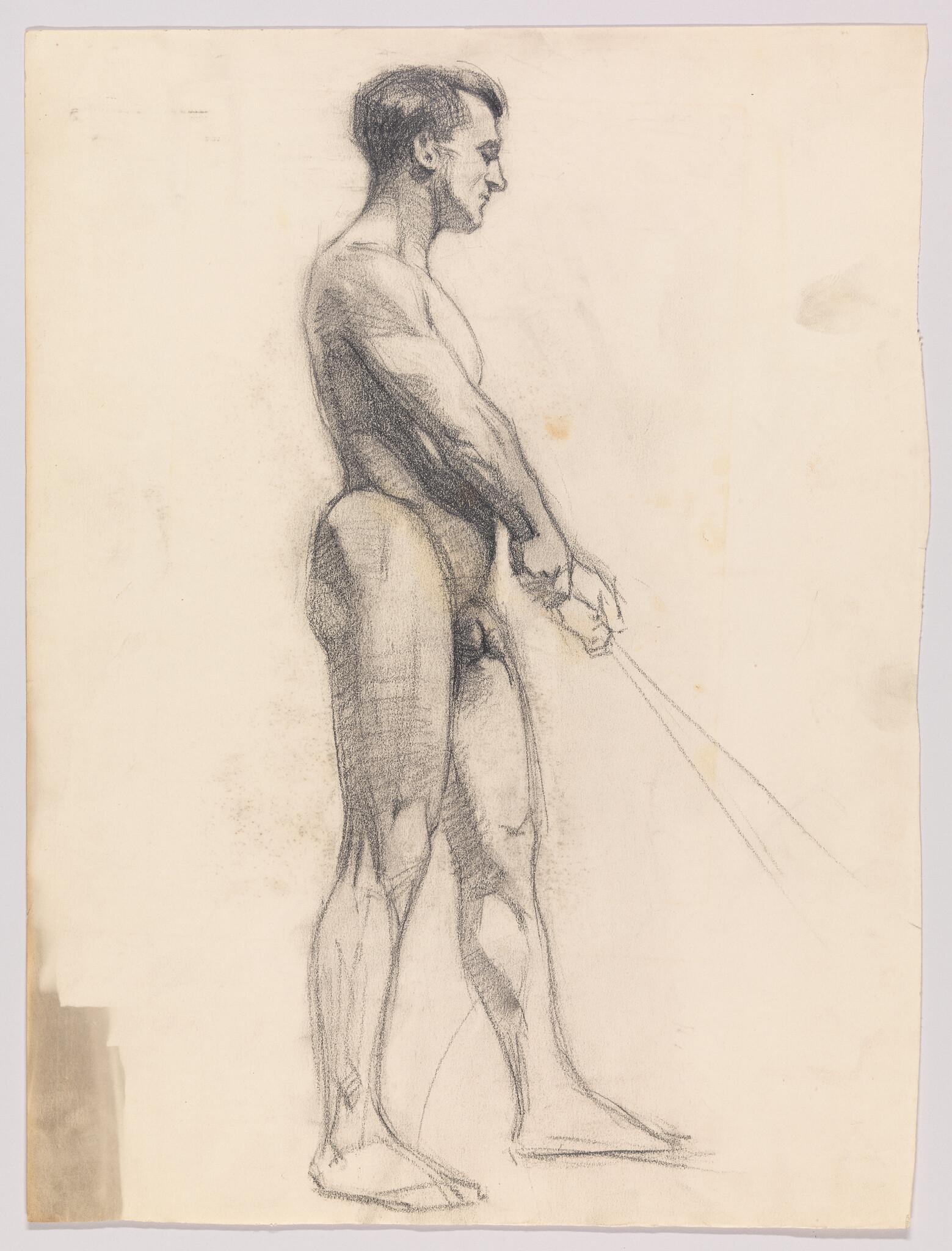 A standing nude male figure drawn in charcoal, seen in right-side profile with hands clasped.