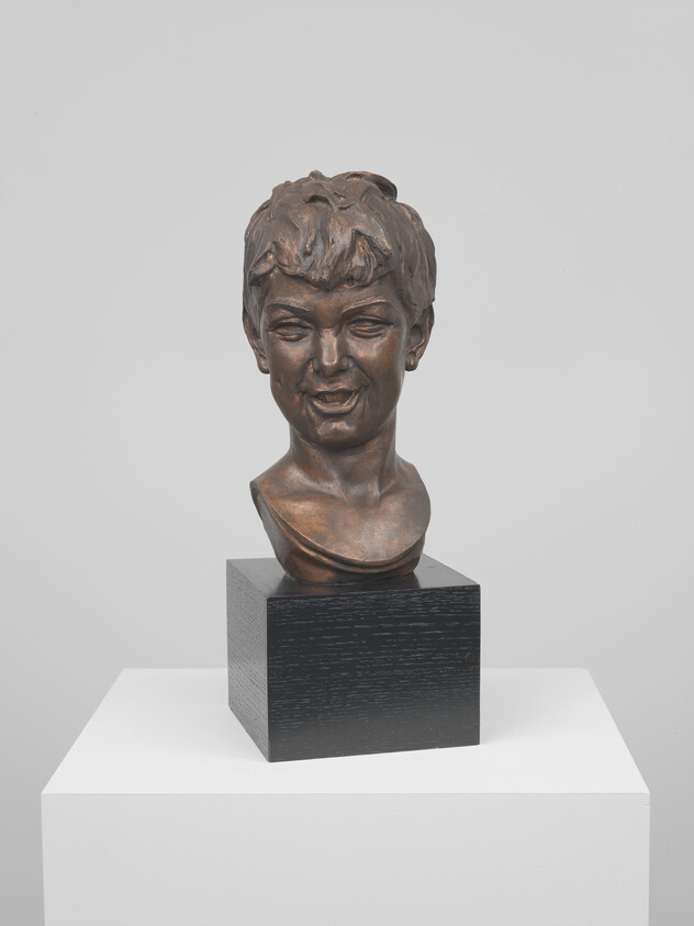 Bronze bust of a smiling young person displayed on a black square pedestal.
