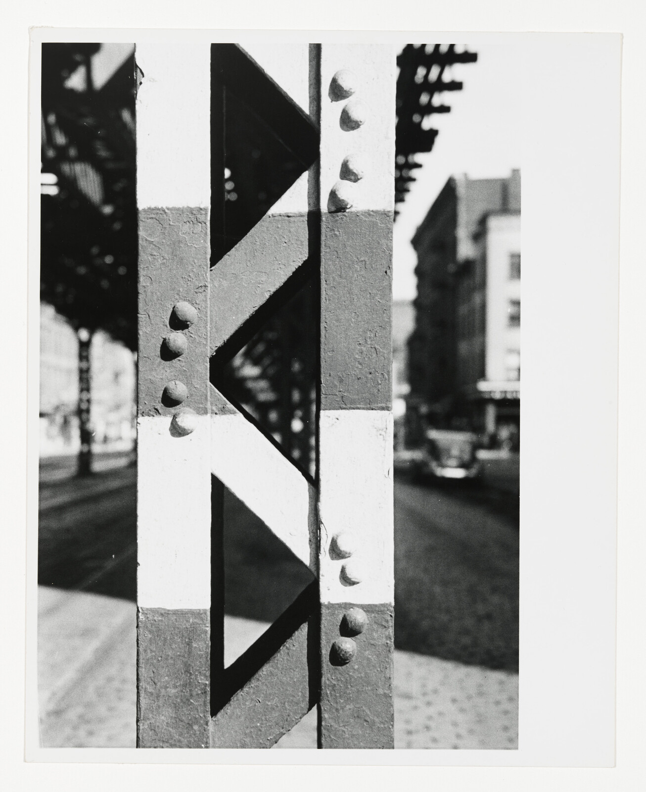 Close-up of a riveted steel support column painted with white stripe under an elevated train.