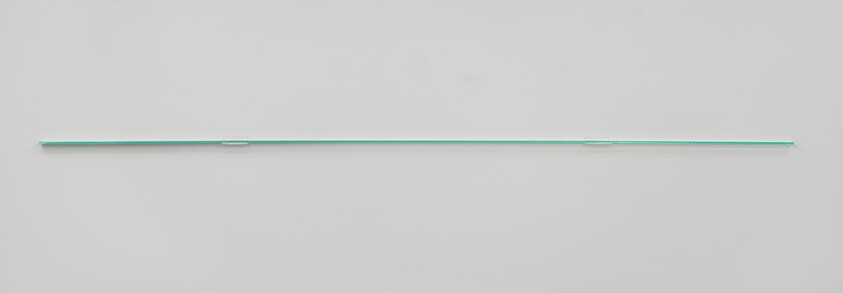 A long thin glass shelf with faint green edge mounted horizontally on a white wall.