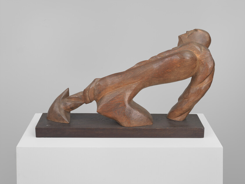A wooden sculpture of a human figure in a dynamic pose, with one arm extended forward and the head tilted upward, displayed on a pedestal against a neutral background.