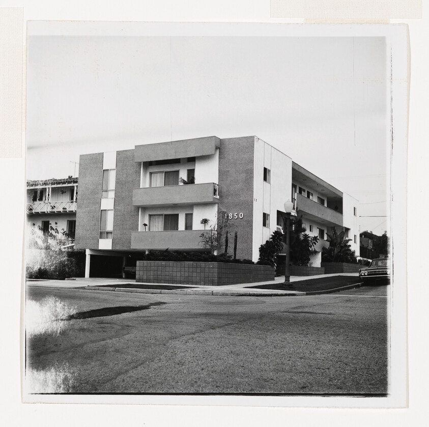 Three-story apartment building with balconies and address number 1850 on a quiet street.