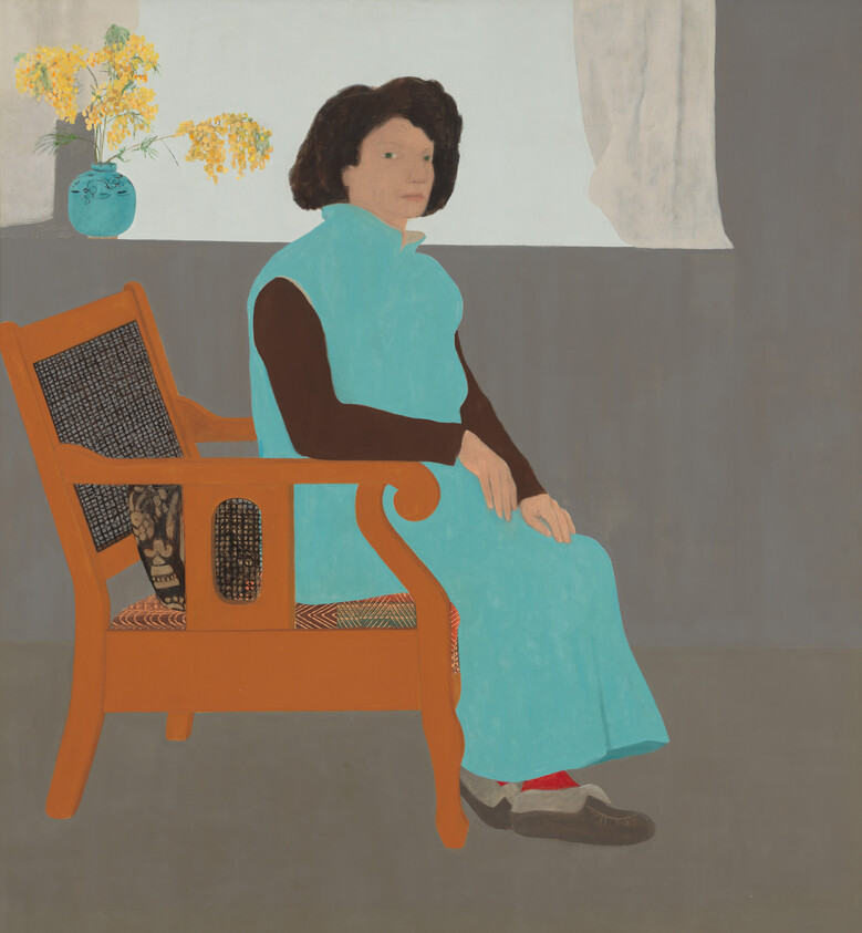 A person in a blue dress sits on an orange chair, with a vase of yellow flowers nearby.