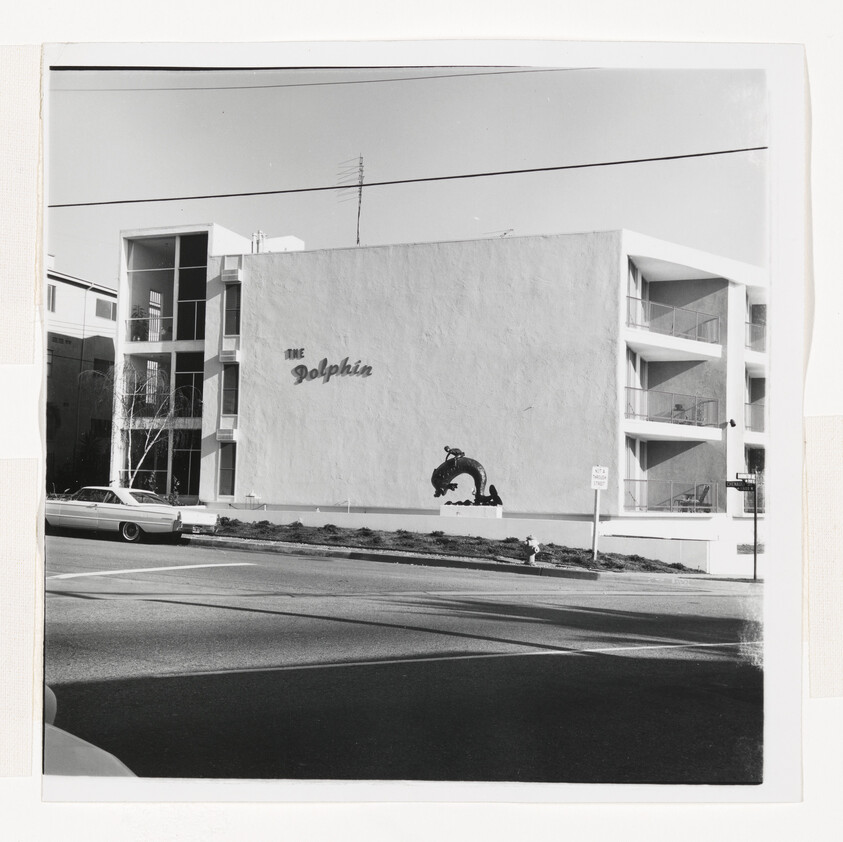 The Dolphin apartment building with a large dolphin sculpture and a parked car on the street.