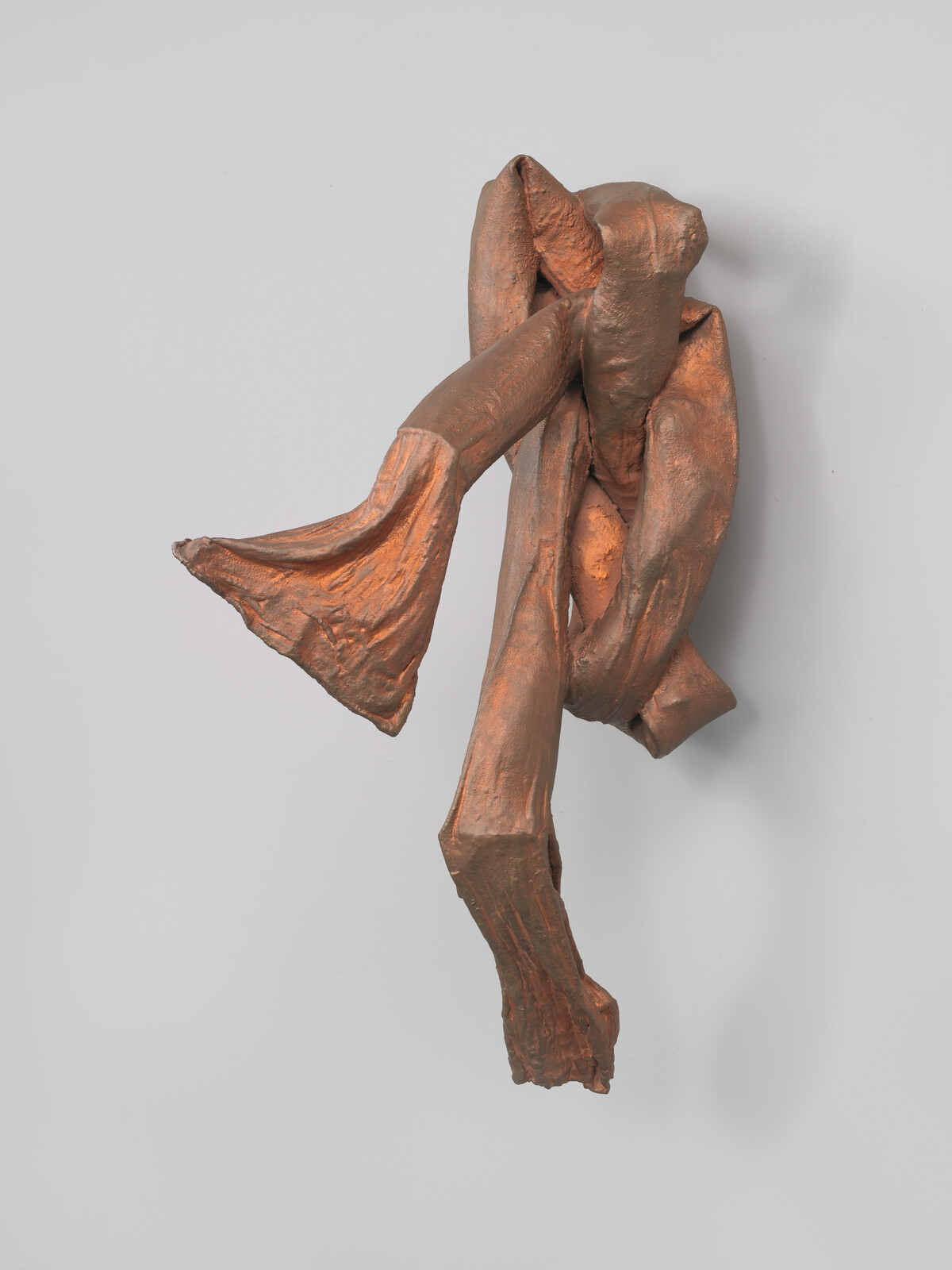 A bronze-colored abstract sculpture hangs on the wall with twisted, folded, limb-like forms.