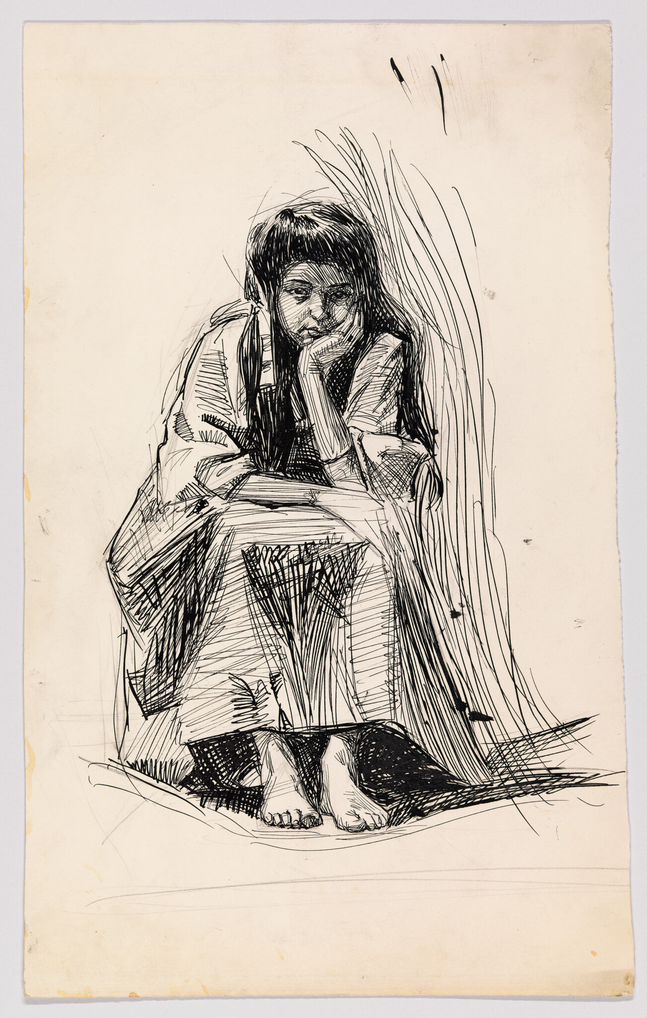 A barefoot person sits hunched forward, resting their chin on their hand and looking thoughtful.